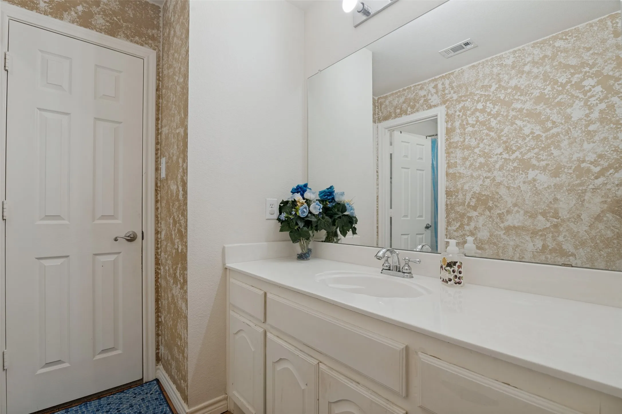White paneled door, built-in vanity with white cabinetry, integrated sink, and a large wall-mounted mirror