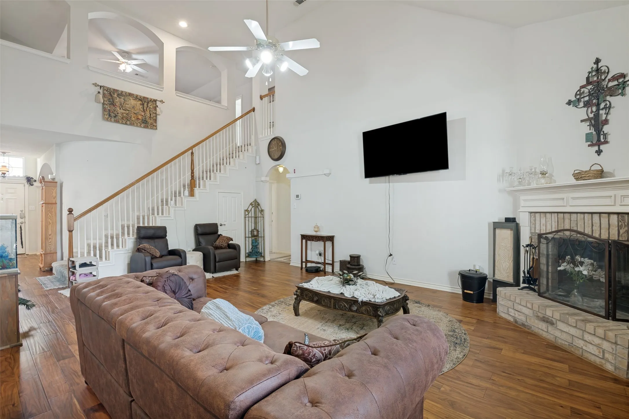 Vaulted ceiling, wood-finish flooring, staircase with wood handrail, brick-surround fireplace with mantel, and ceiling fan with integrated lighting