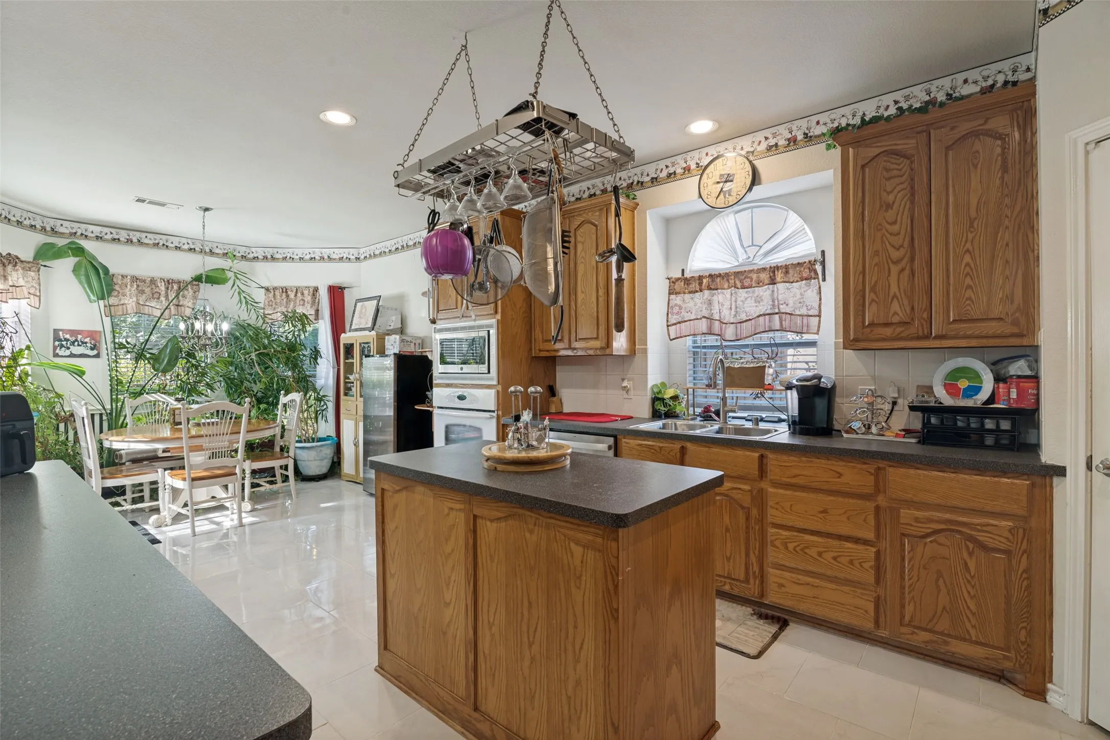 Kitchen featuring wood-finish cabinetry, a central island with a solid surface countertop, double basin sink, and built-in wall oven
