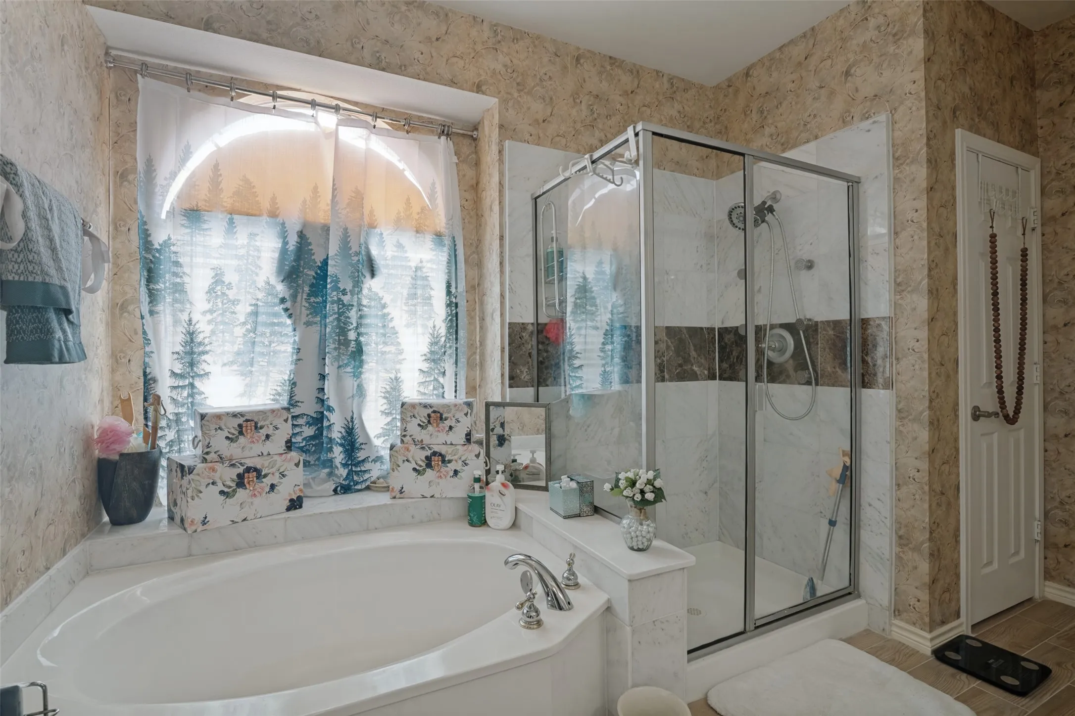 Recessed corner soaking tub with a tiled surround, glass-enclosed shower with a tiled interior, and stone-look wall finishes