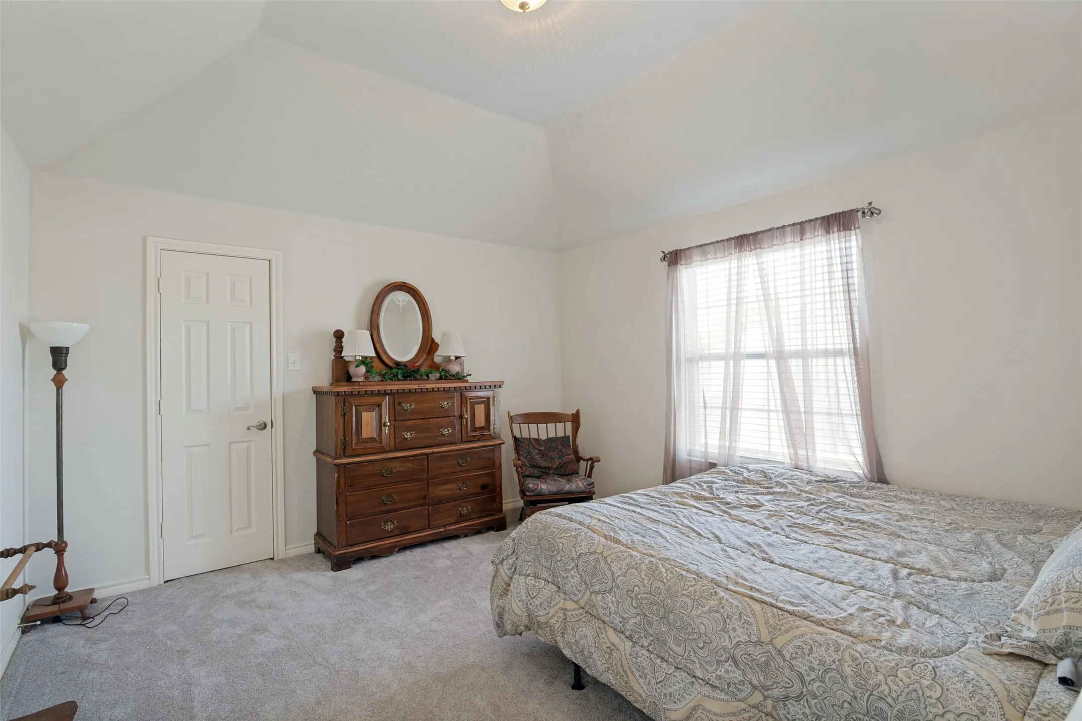 Vaulted ceiling, white painted walls, natural light from window, white paneled door, light-colored carpeting