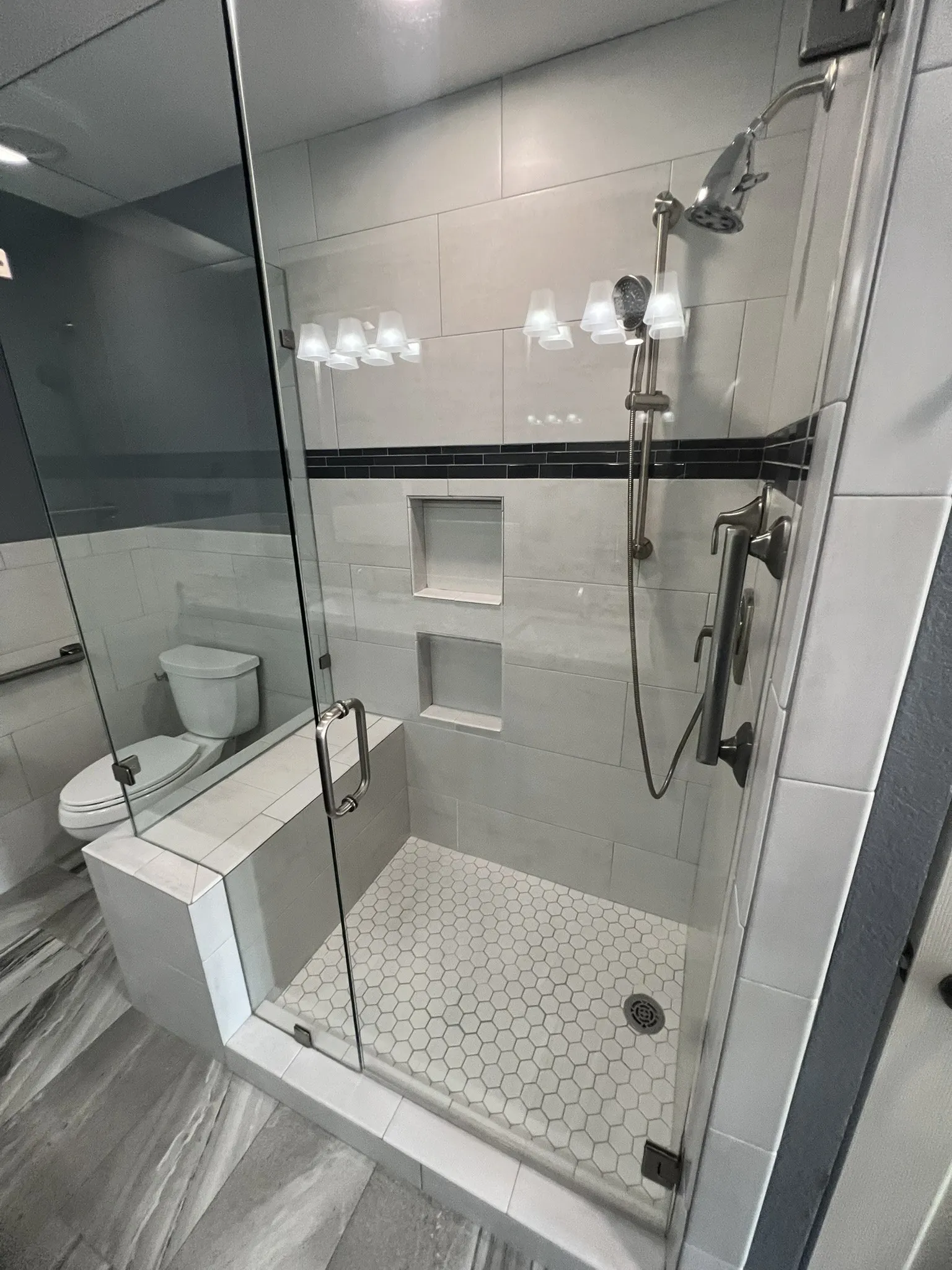 Master Bathroom Glass-enclosed shower with white hexagon tile flooring, dual shower heads, and built-in shelving