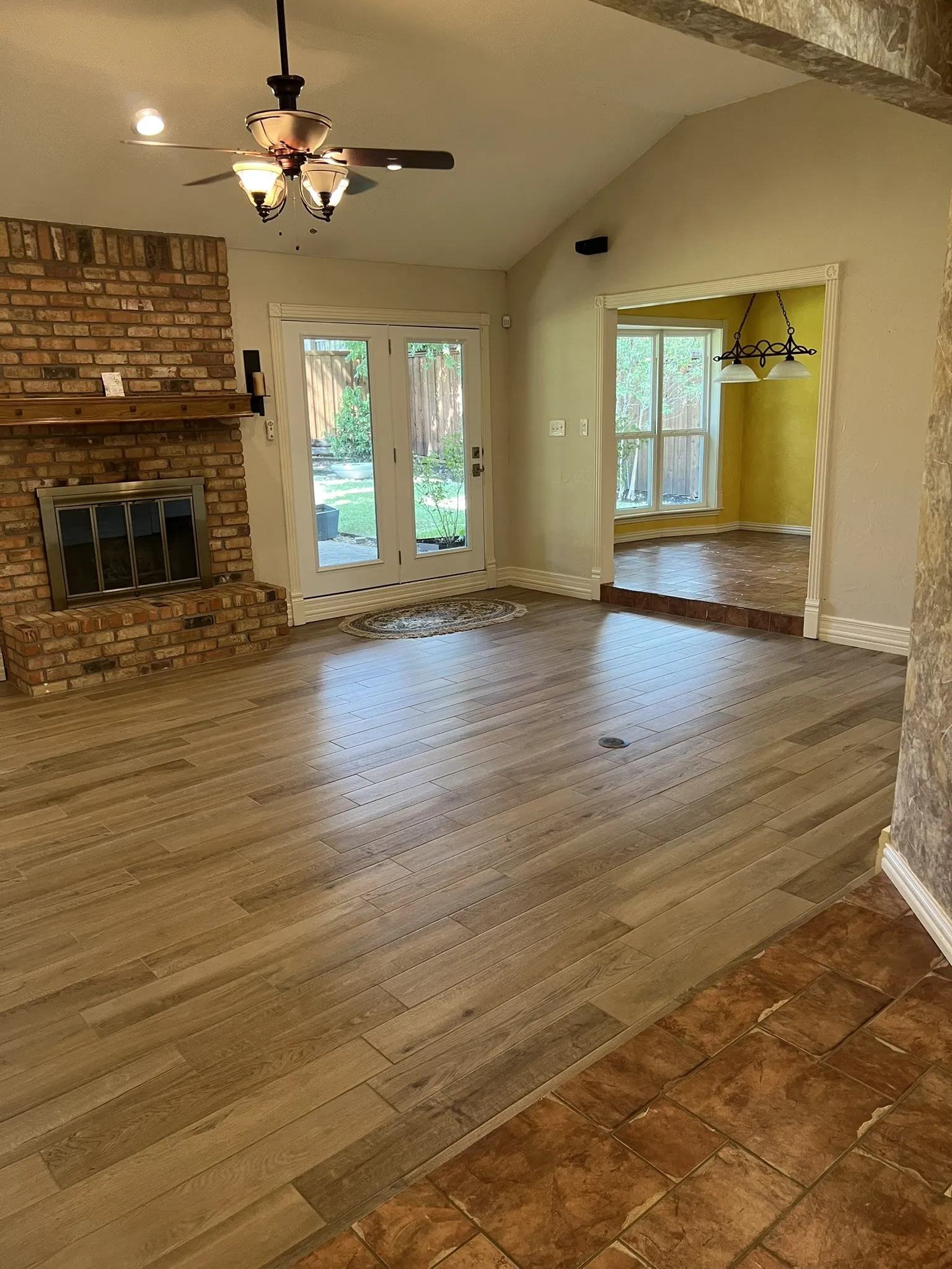Vaulted ceiling with a ceiling fan, brick fireplace with a wood mantel, wood-finish flooring, and French doors