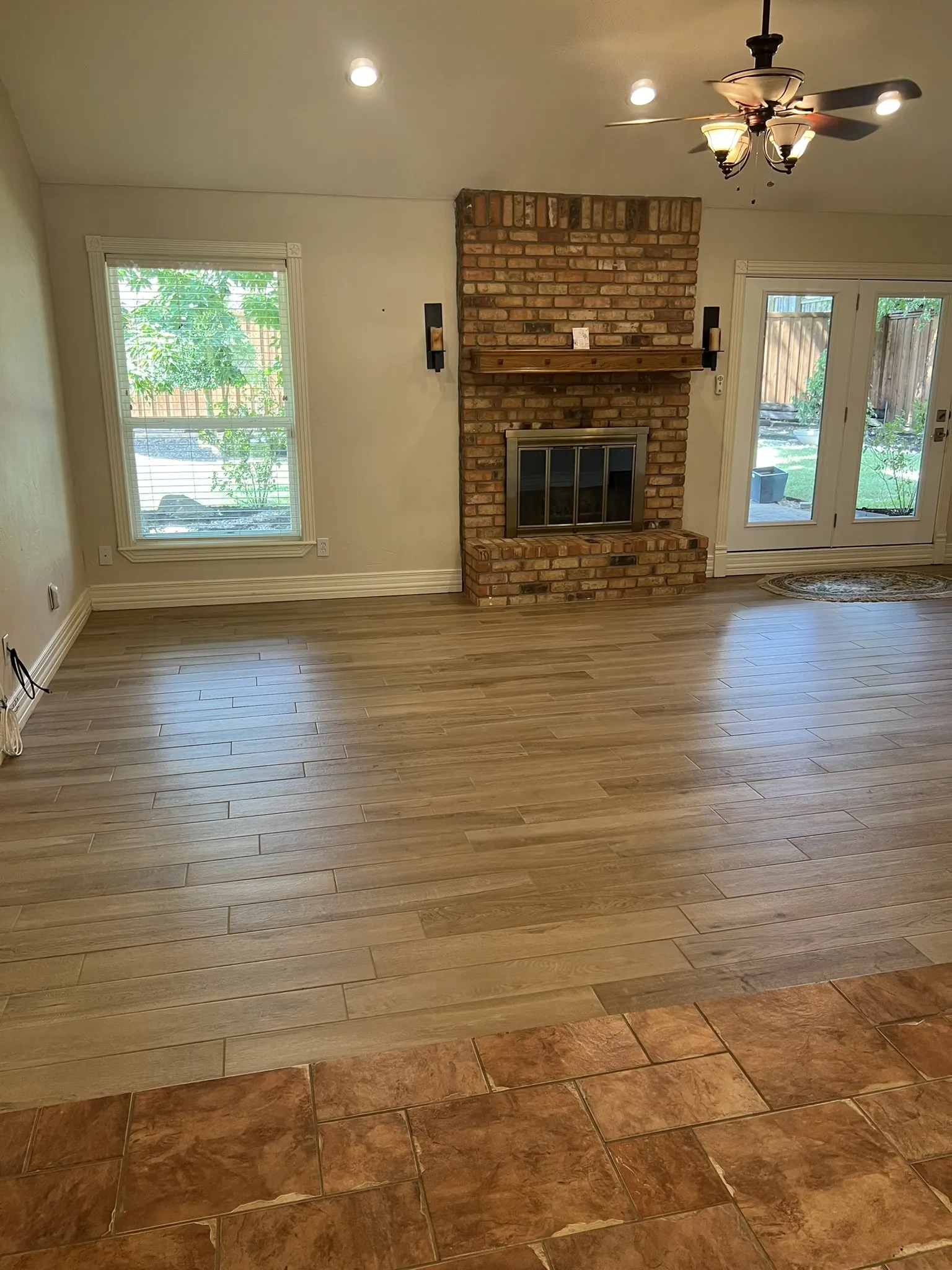 Brick fireplace with wood mantel, French doors, recessed lighting, and wood-finish flooring
