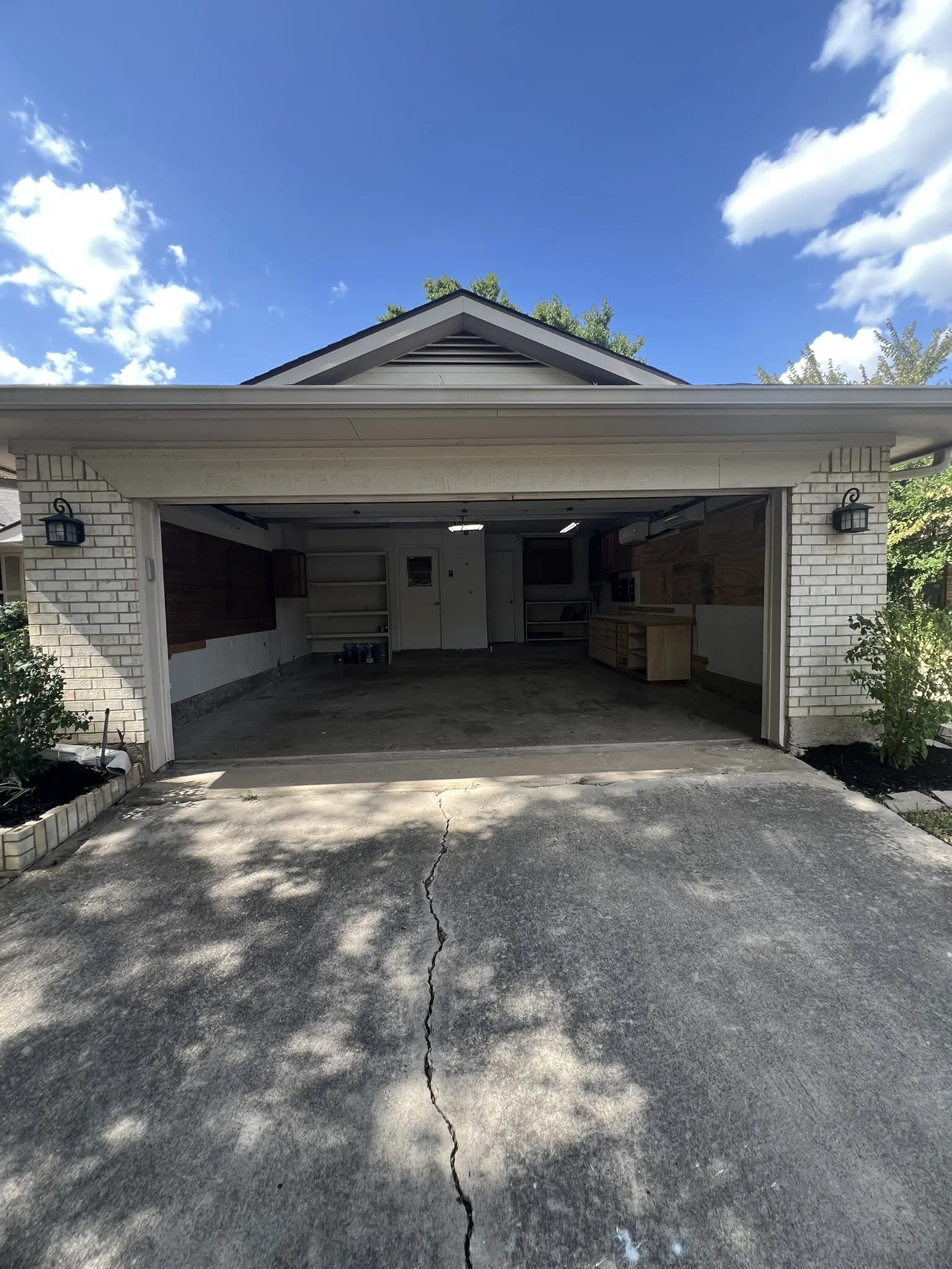 Attached garage with light-colored brick exterior, decorative outdoor wall sconces, and a gable roofline