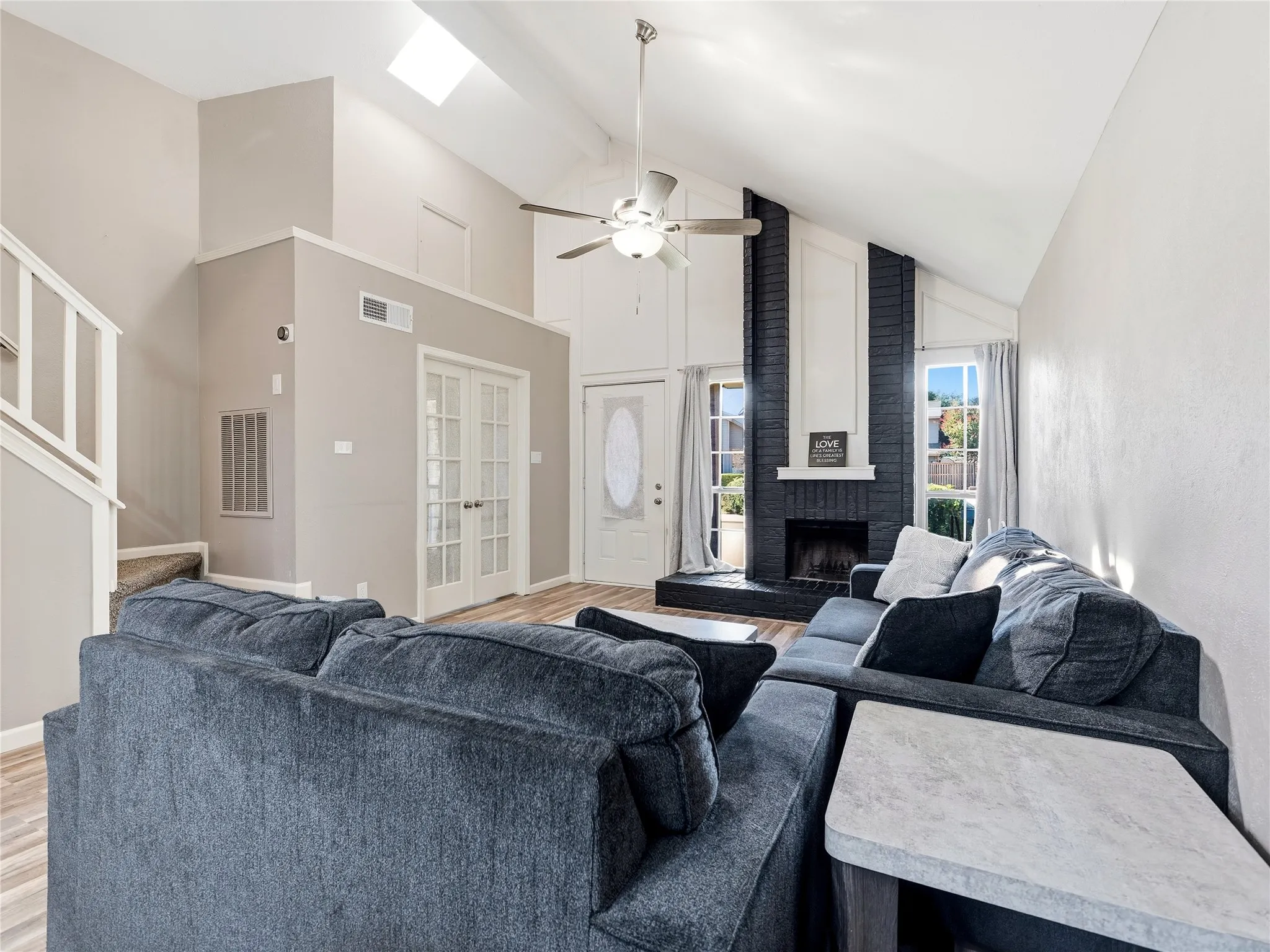 Vaulted ceiling with skylight, wood-finish flooring, and a dark brick fireplace with a white mantle