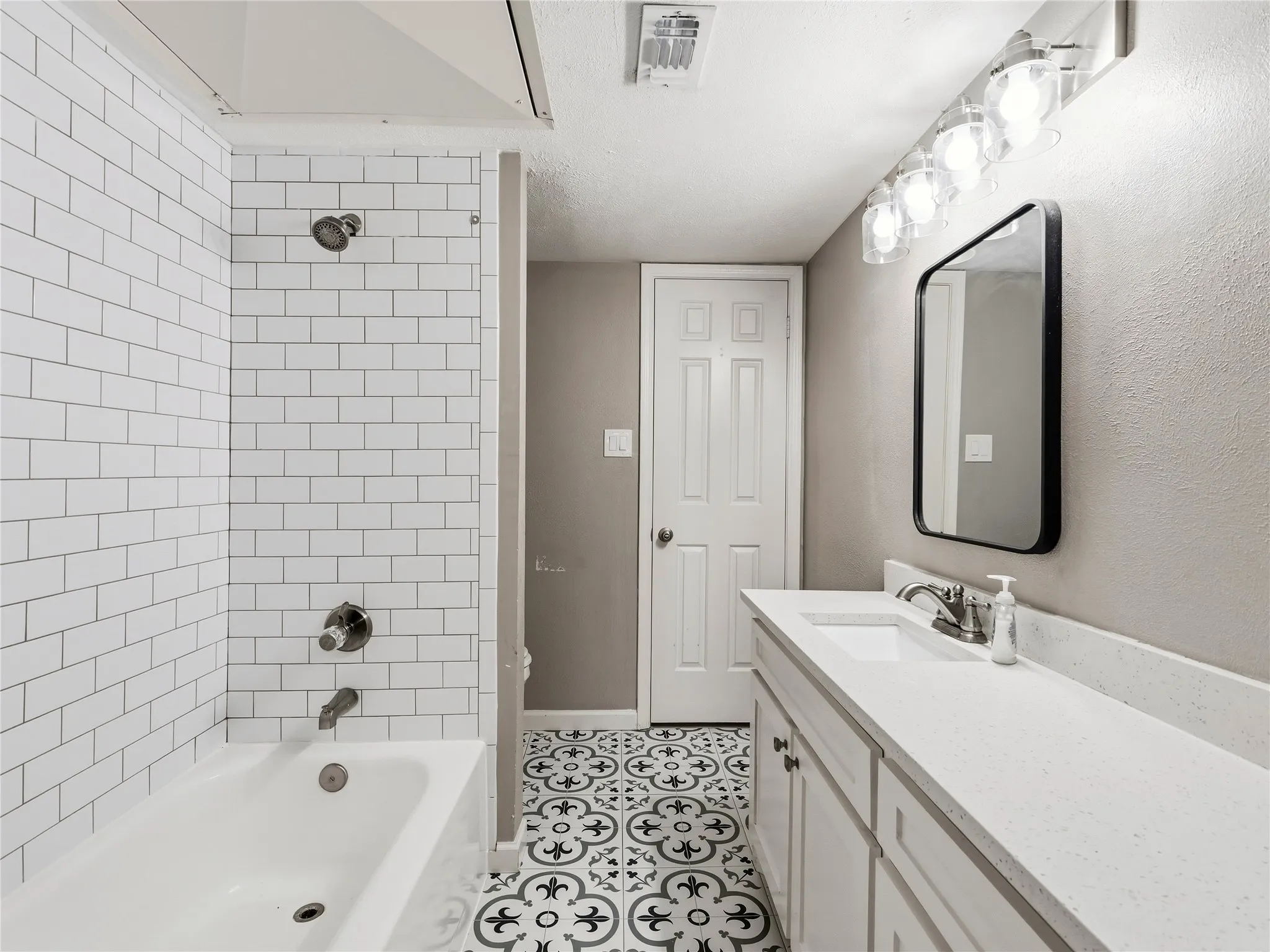 Shower-over-tub combination with white subway tile surround, vanity with single basin sink and white countertop, and patterned floor tile