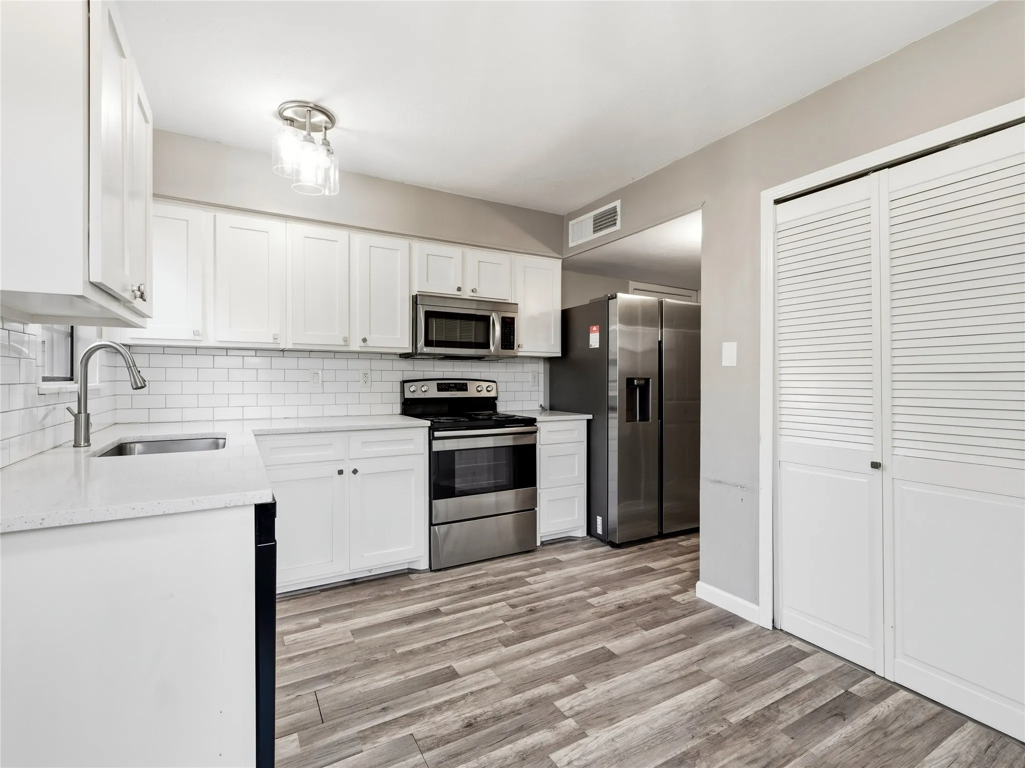 White shaker cabinetry, stainless steel appliances, subway tile backsplash, light-toned wood-finish flooring, and white louvered closet doors