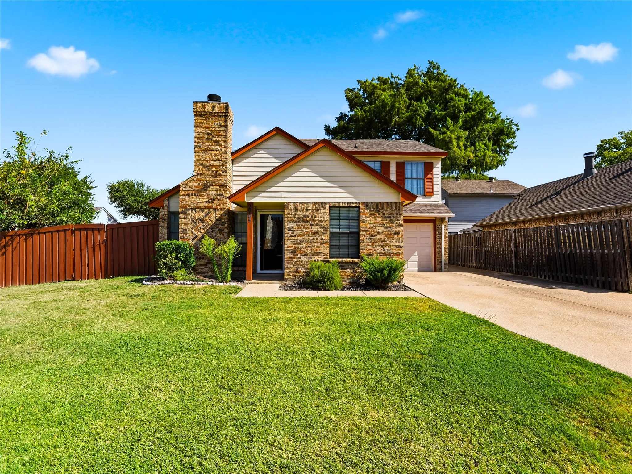 Brick and siding exterior, prominent brick chimney, attached garage, concrete driveway, and a fenced perimeter