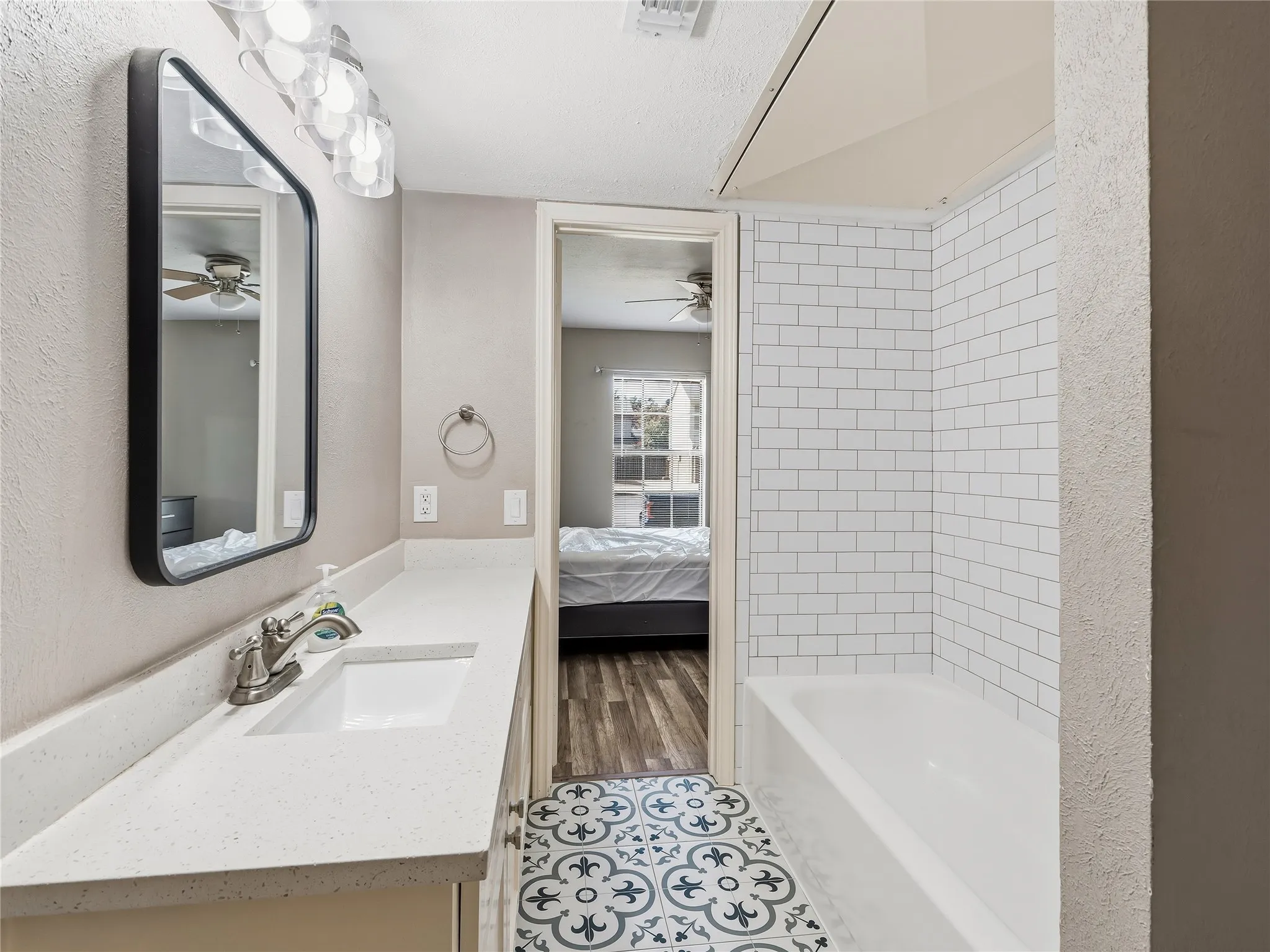 Full bathroom featuring a single vanity with a white countertop and integrated sink, a rounded rectangular mirror, and a full-size bathtub with white subway tile surround