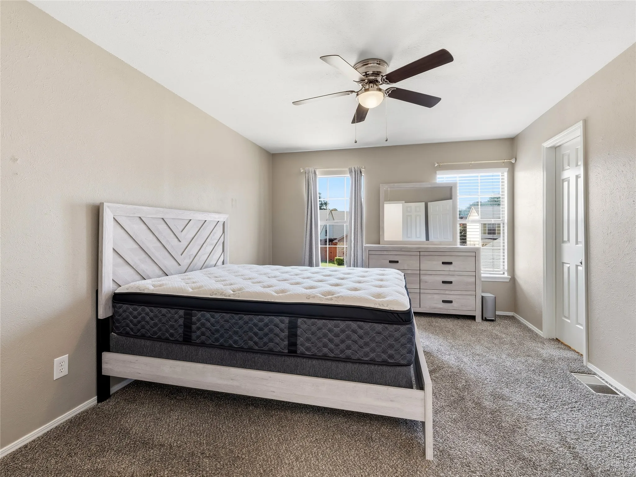 Plush carpeting throughout, ceiling fan with light fixture, multiple windows with blinds, and painted interior door