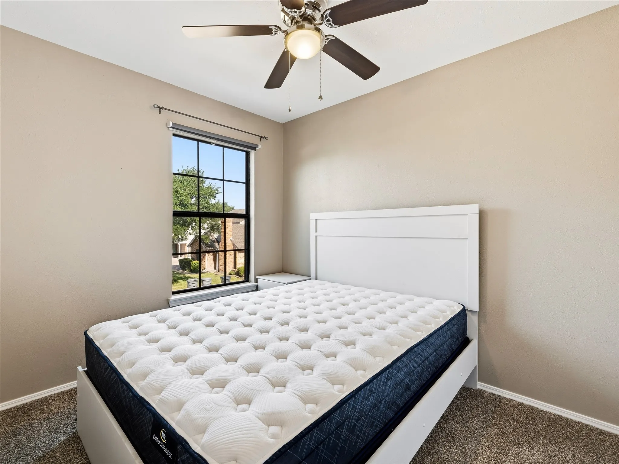 Neutral-toned walls, a multi-pane window with roller blinds, a ceiling fan with integrated lighting, and carpeted flooring