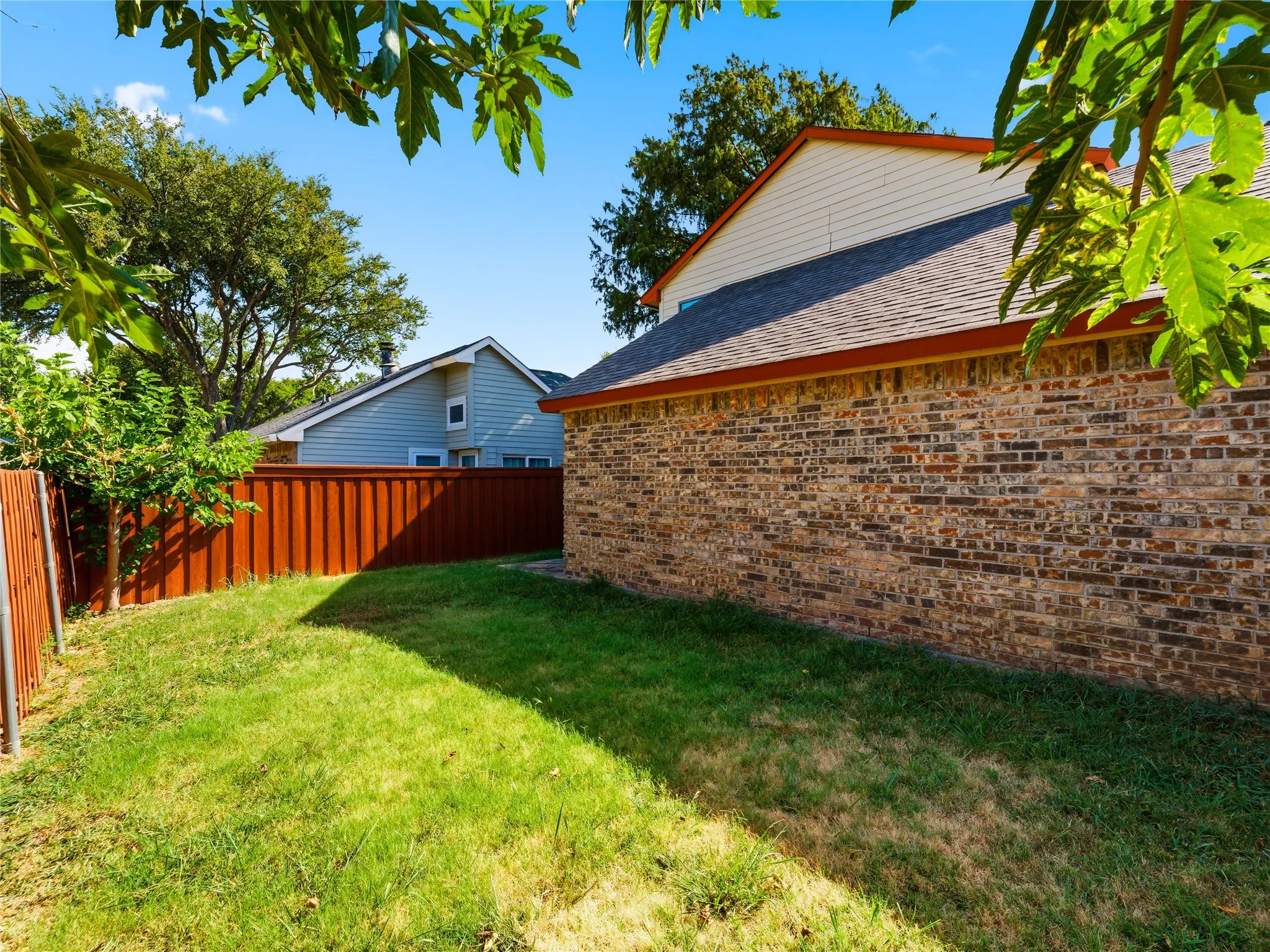 Expansive lawn area featuring a brick exterior wall, sloped roofline, and a privacy fence