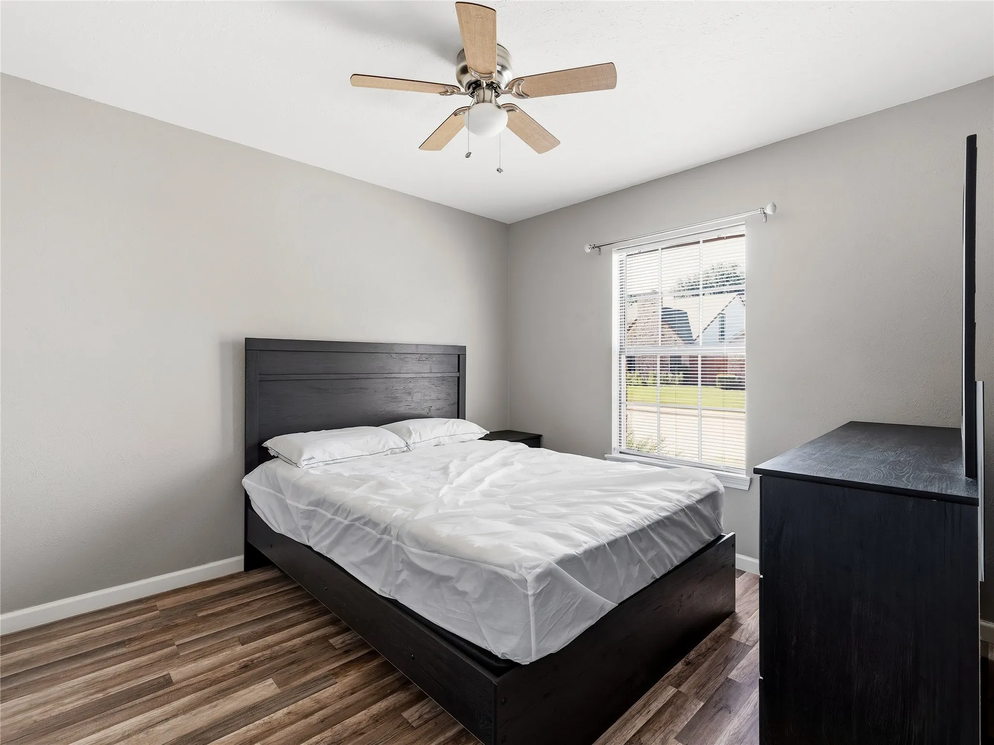 Wood-finish flooring with a neutral wall color, a ceiling fan with light fixture, and a window providing natural light