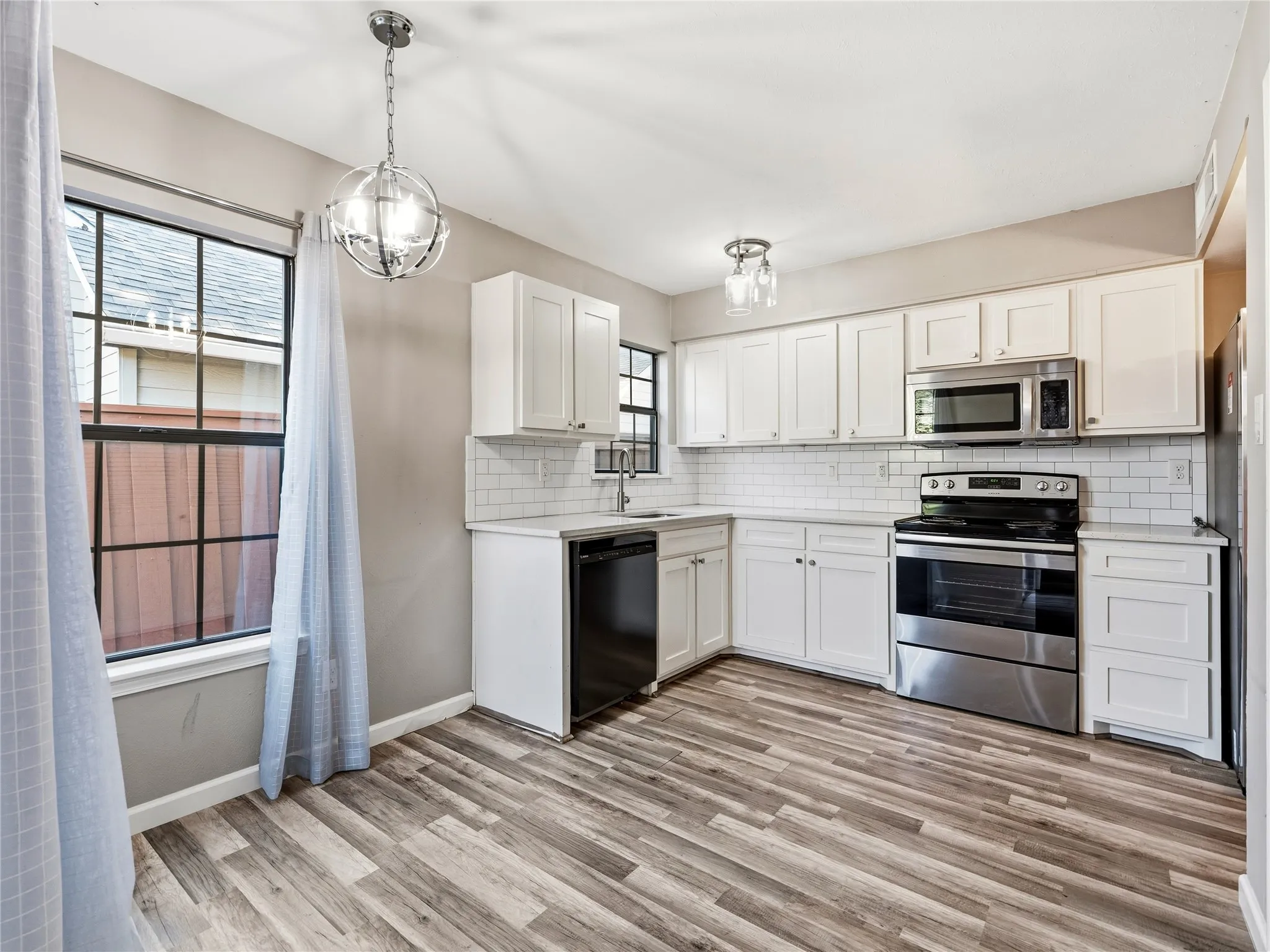 Kitchen featuring white shaker cabinetry, stainless steel appliances, subway tile backsplash, wood-finish flooring, and a window with grid detailing