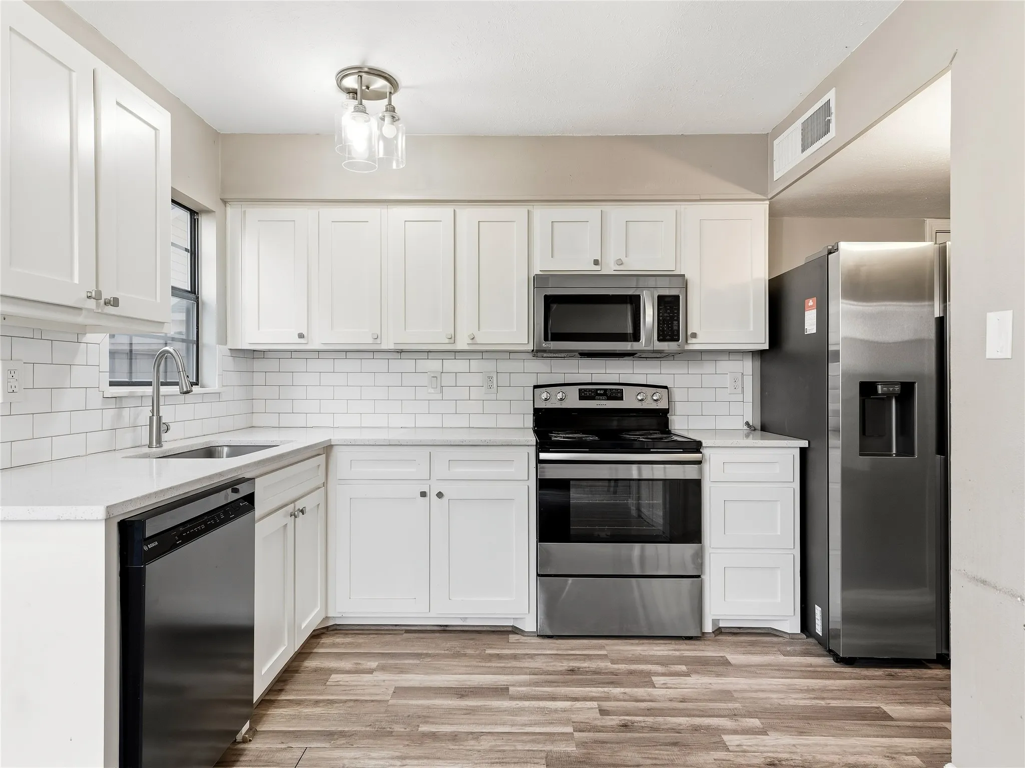 Kitchen featuring white shaker-style cabinetry, stainless steel appliances, a subway tile backsplash, light-toned countertops, and wood-finish flooring