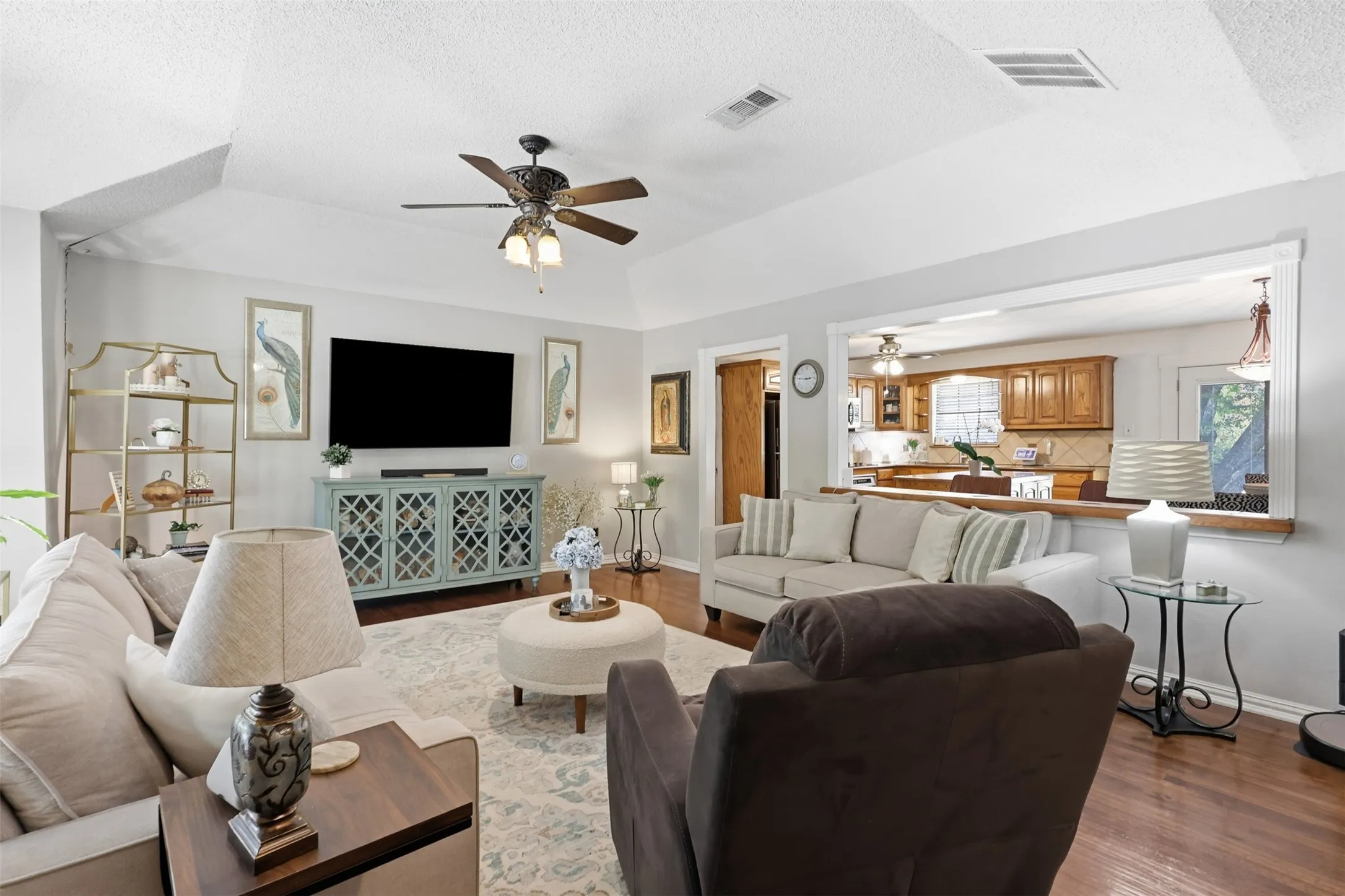 Recessed ceiling, ceiling fan with integrated lighting, hardwood flooring, neutral wall tones, and pass-through opening