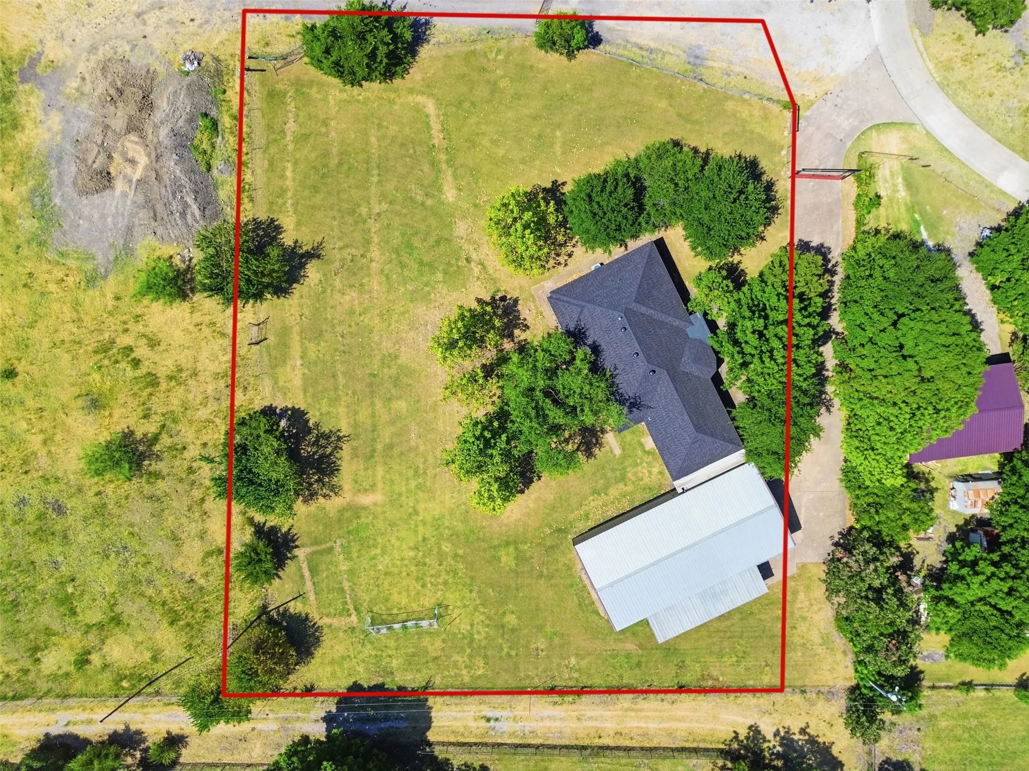 Expansive property featuring a primary residence with a dark shingle roof, a secondary structure with a metal roof, and abundant mature trees