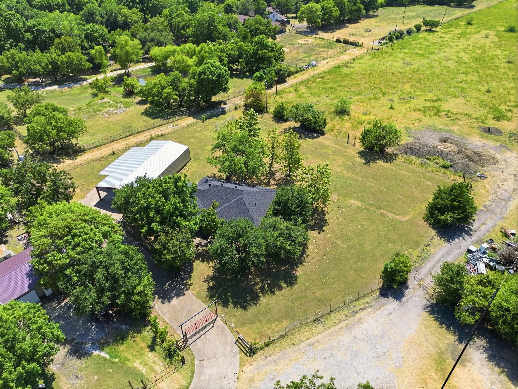 Expansive property featuring a gated entrance, asphalt driveway, mature trees, a metal outbuilding with an attached carport