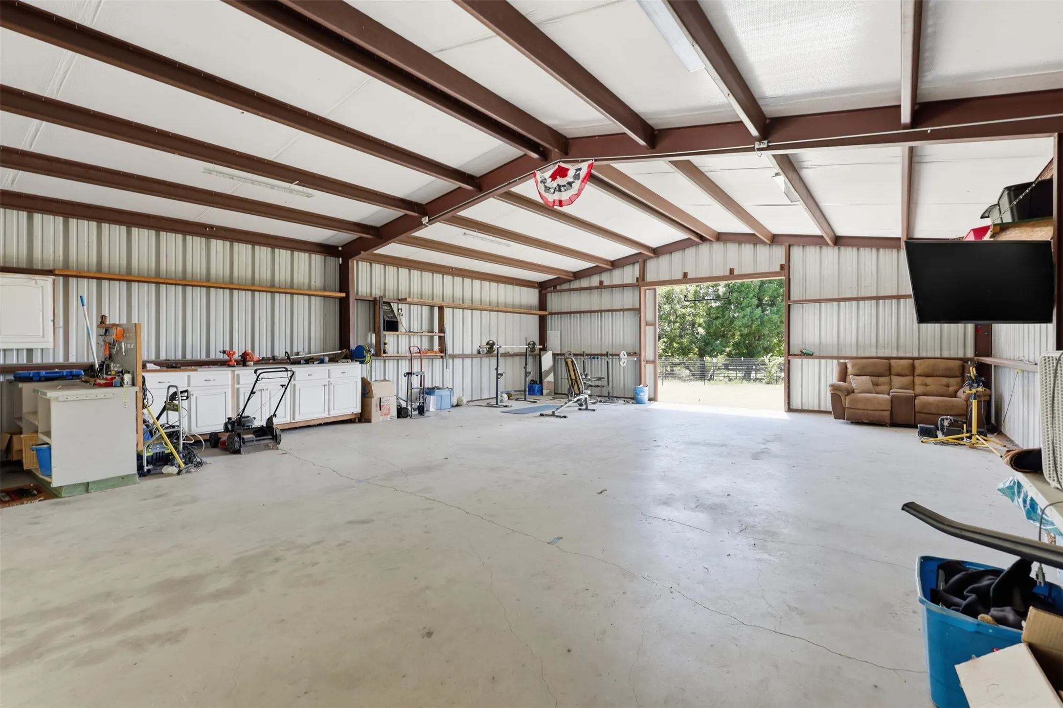 Spacious metal structure featuring a concrete floor, exposed beam ceiling, and built-in white cabinetry