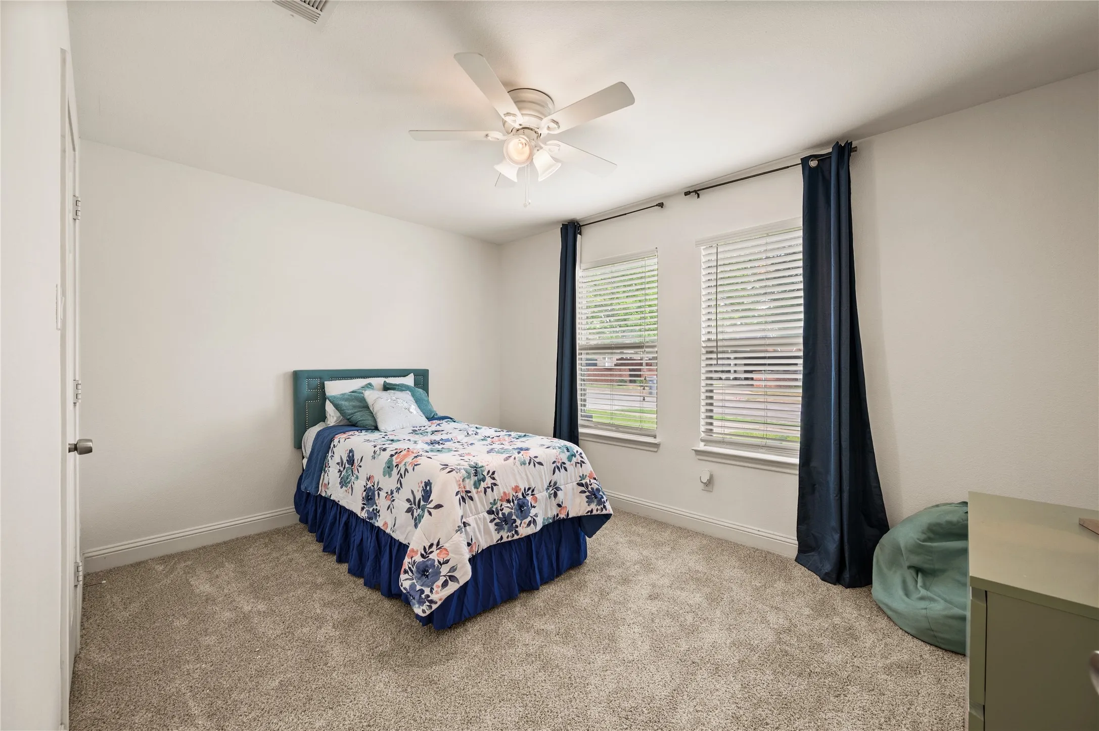 Carpeted room featuring dual windows, a ceiling fan with integrated lighting, and neutral wall tones