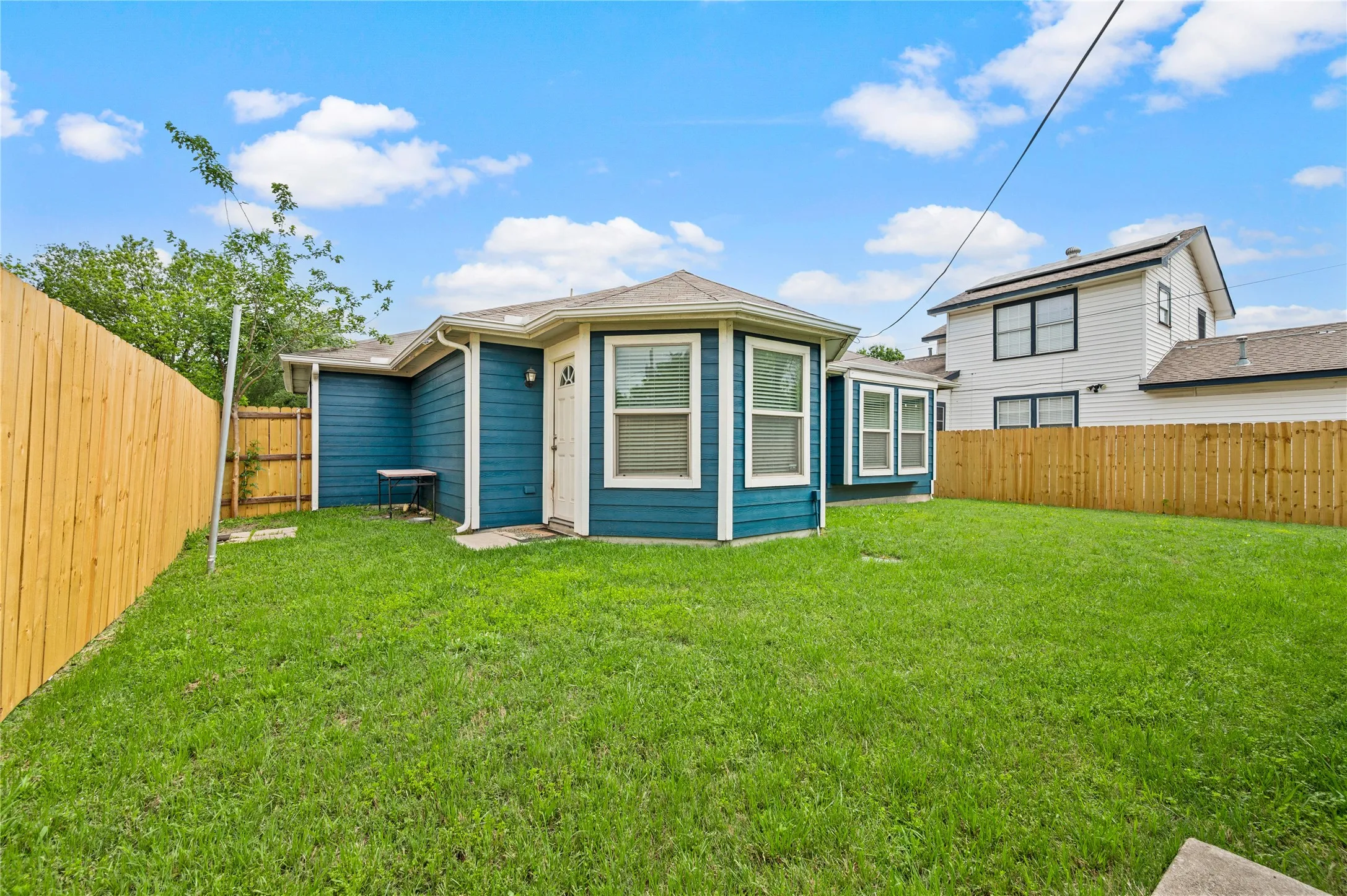 Expansive grassy backyard featuring newly installed perimeter fencing and a blue siding exterior with white trim