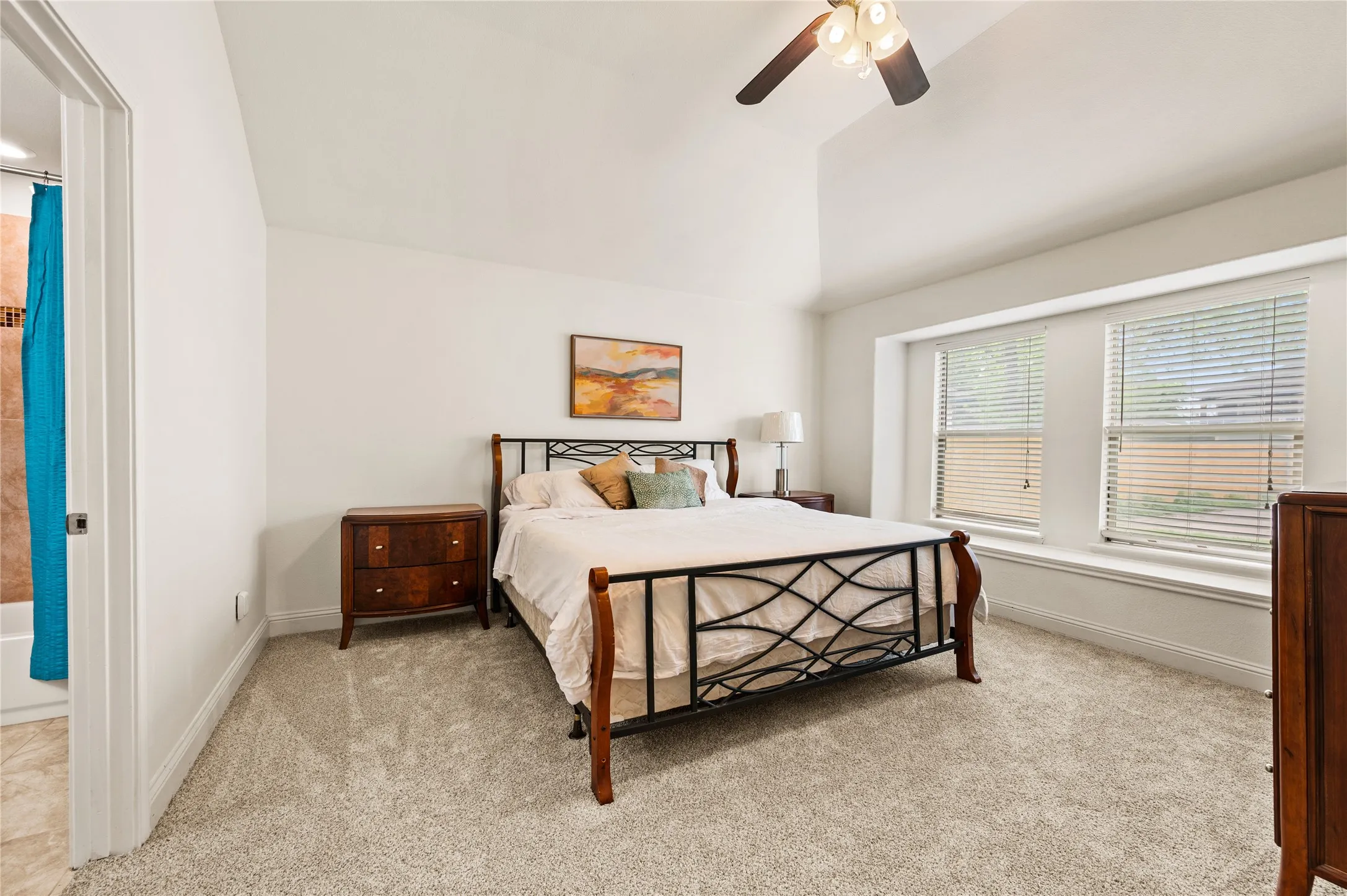 Vaulted ceiling with ceiling fan, expansive carpeted flooring, large window with integrated window seating, and an attached full bathroom with shower and tub combination