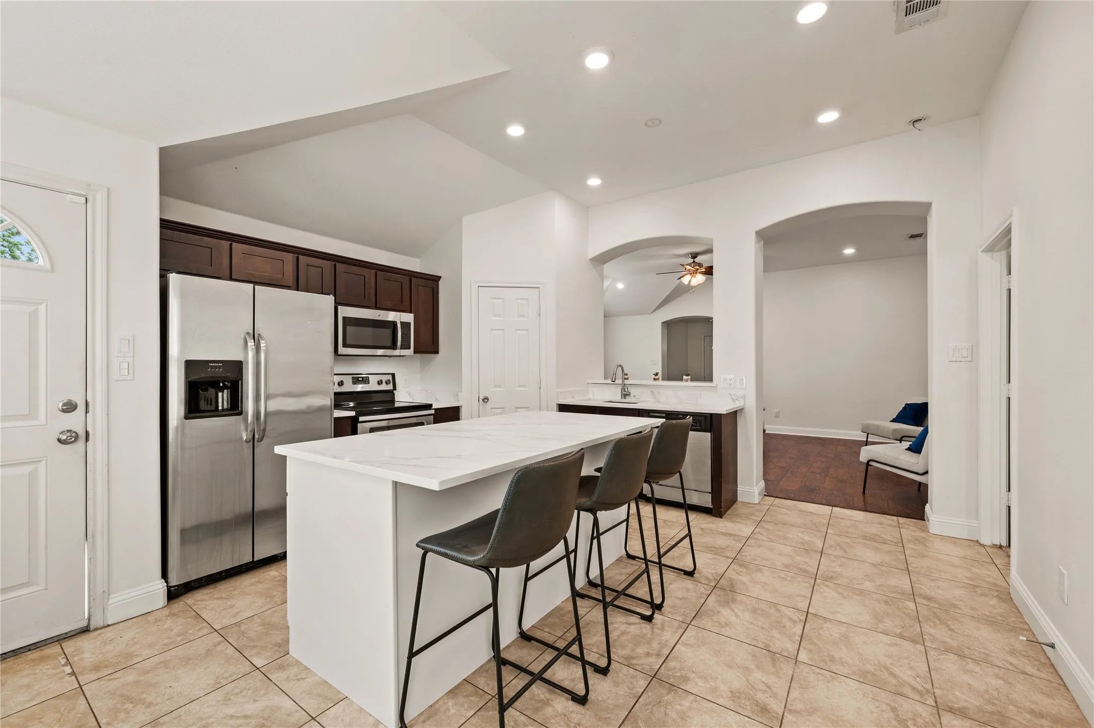 Kitchen featuring a white countertop island, stainless steel appliances, dark wood cabinetry, recessed lighting, and tile flooring