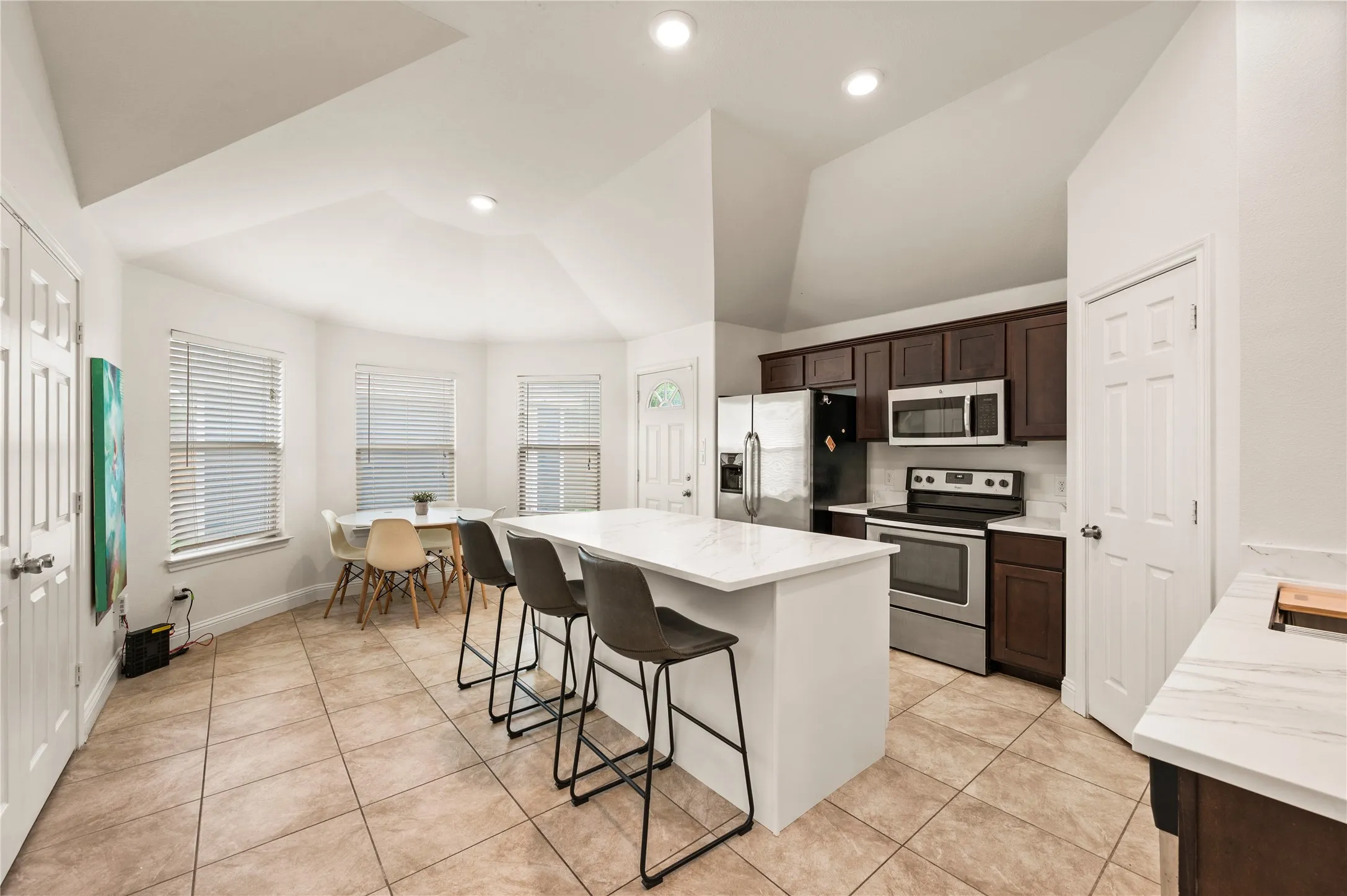 Kitchen featuring a center island with a light-toned countertop, stainless steel appliances, dark wood-finish cabinetry, and tile flooring