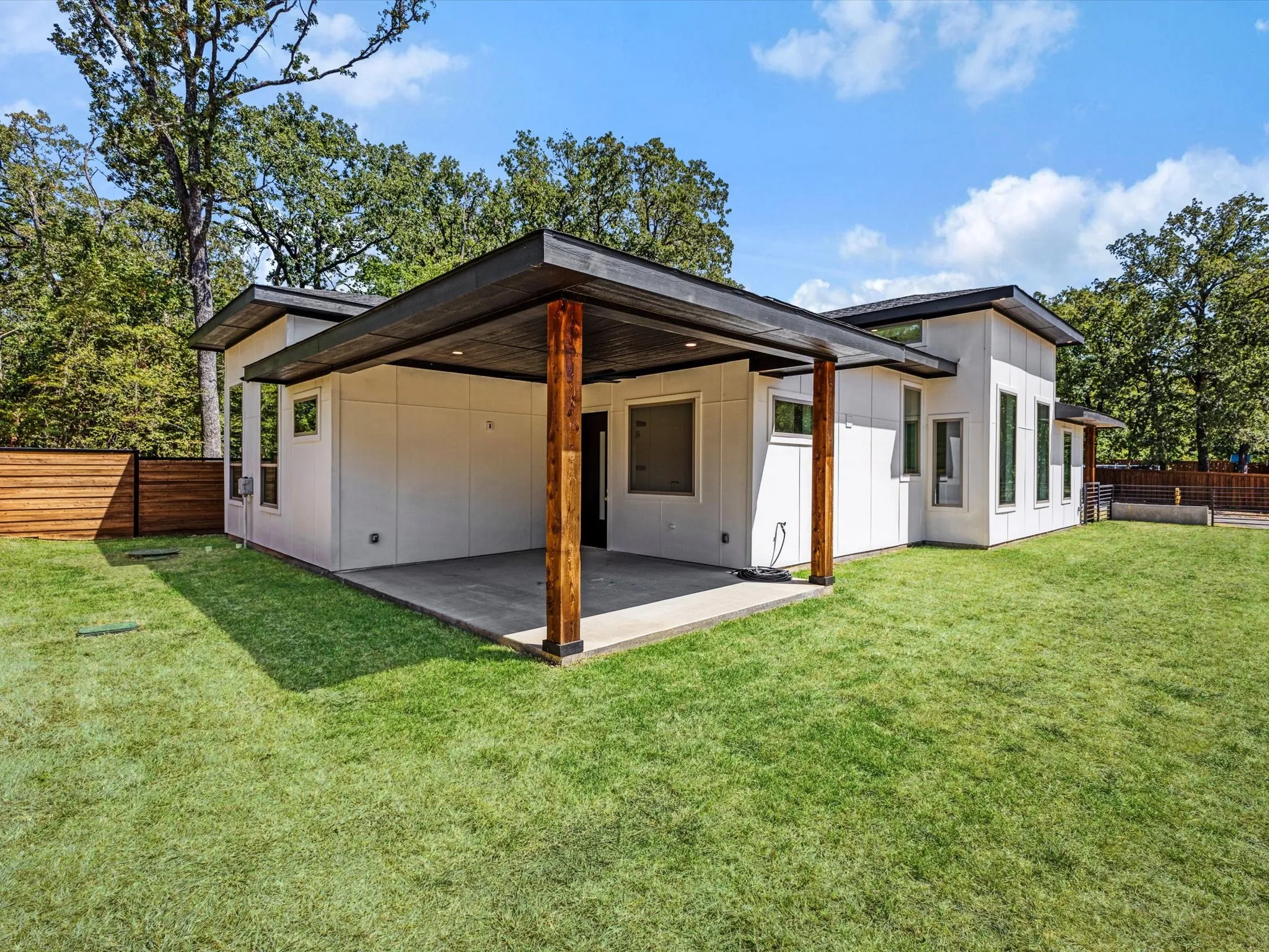Modern exterior with a covered patio, wood-tone accent posts, and a wood privacy fence
