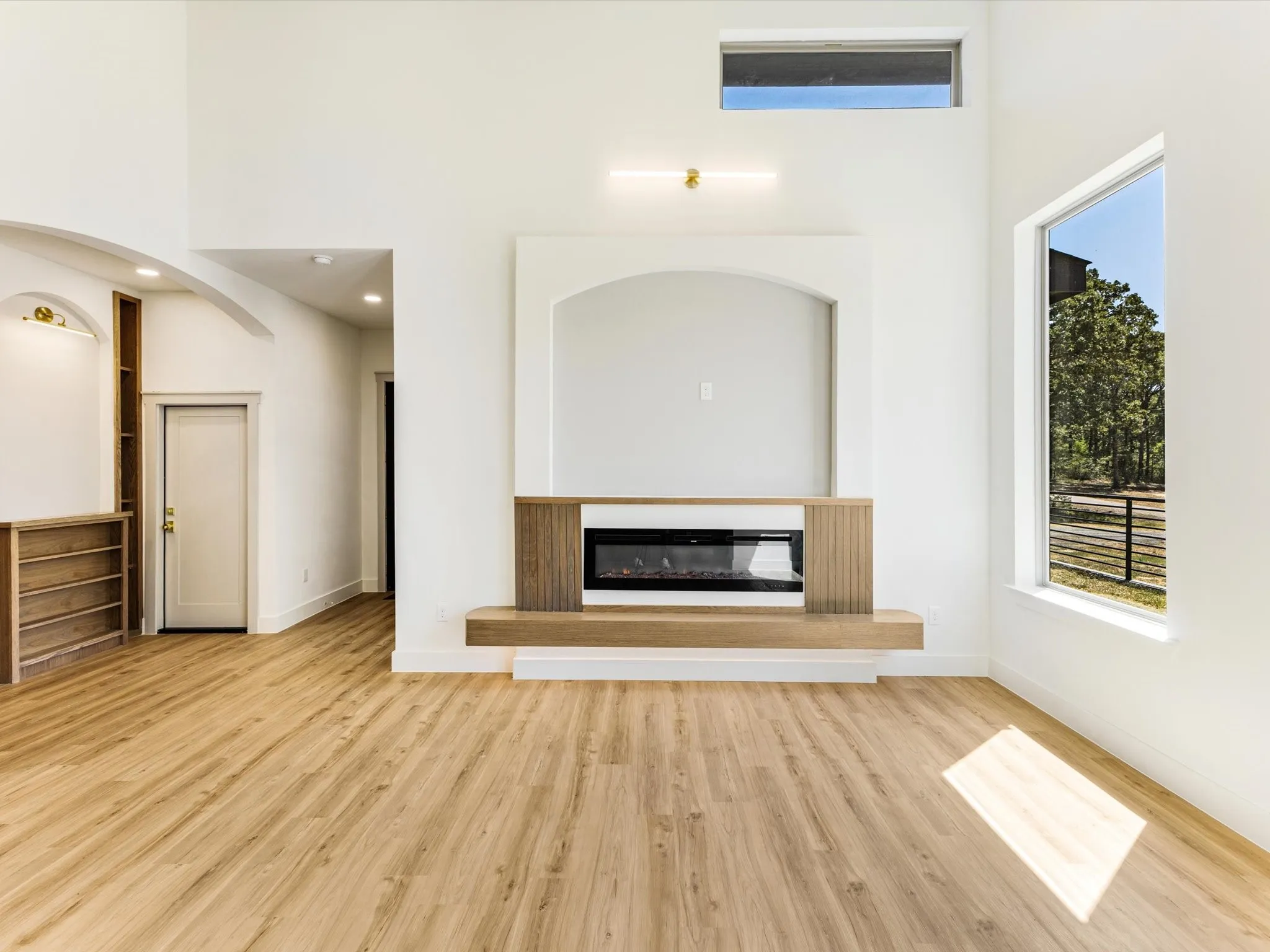 Expansive room featuring high ceilings, wood-finish flooring, a built-in electric fireplace, and large windows