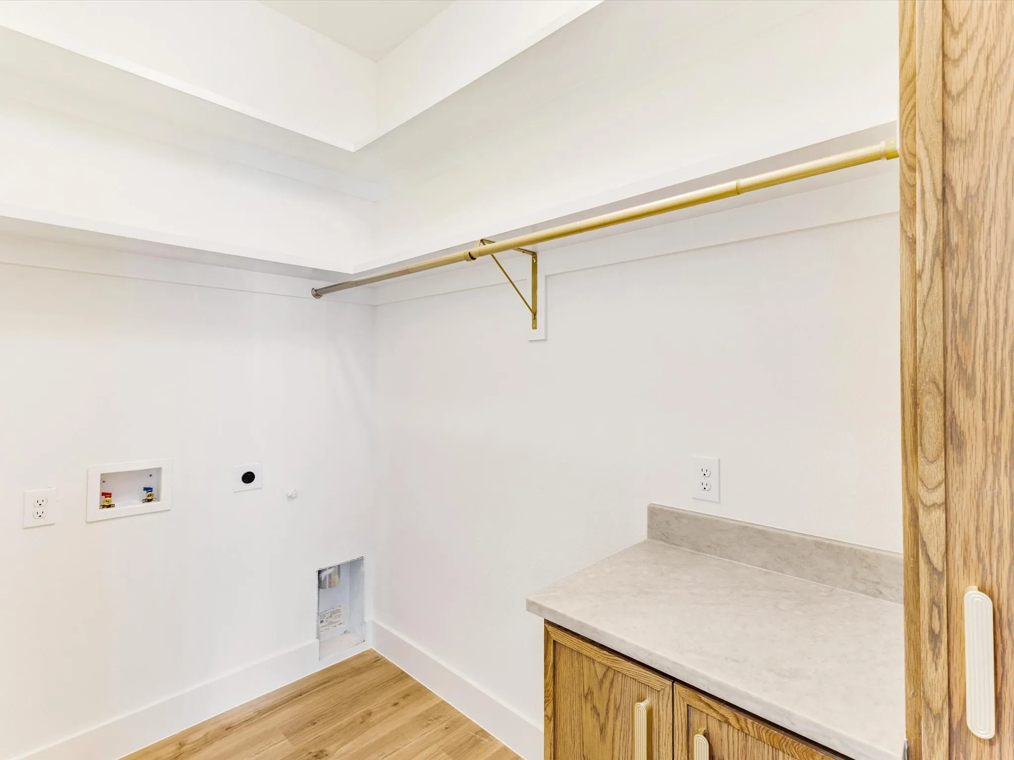 Laundry area featuring light wood-finish flooring, a built-in wood-finish cabinet with a light-toned countertop, and a brass-toned hanging rod