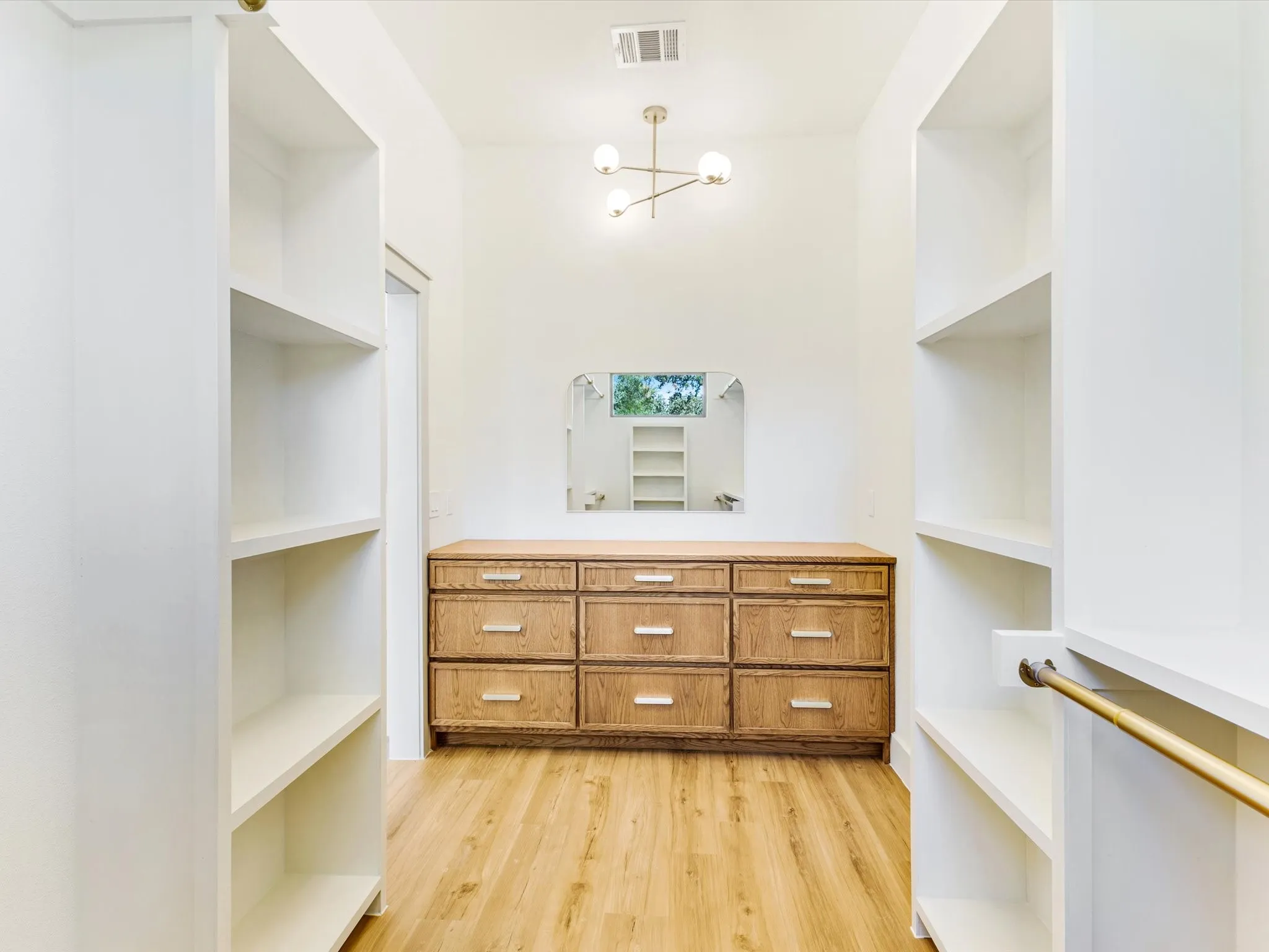 Built-in shelving, wood-finish flooring, recessed lighting, nine-drawer dresser, and a gold-finish chandelier