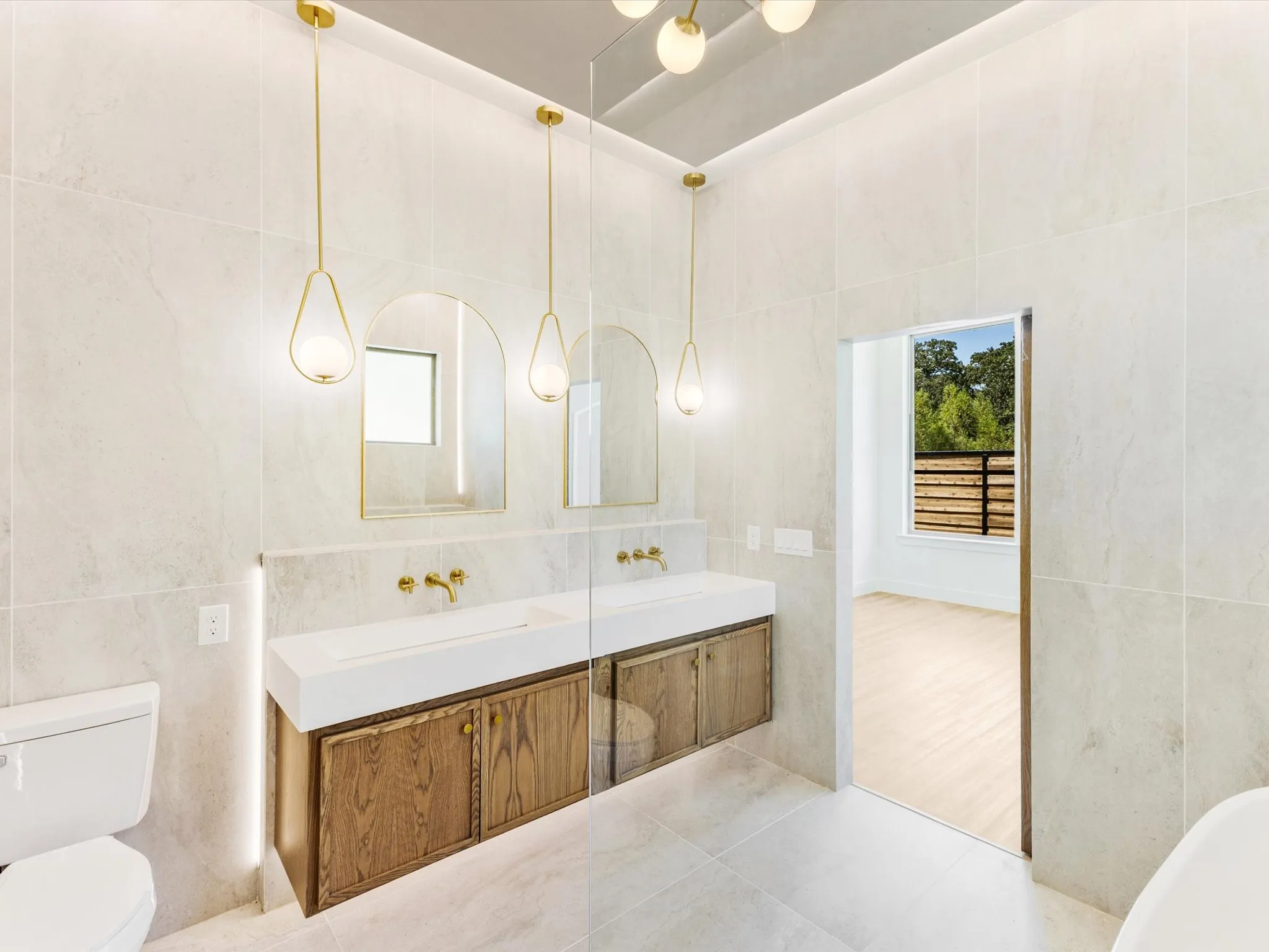 Dual floating vanities with integrated sinks, wood-finish cabinetry, contemporary wall-mounted faucets, arched mirrors, and pendant lighting