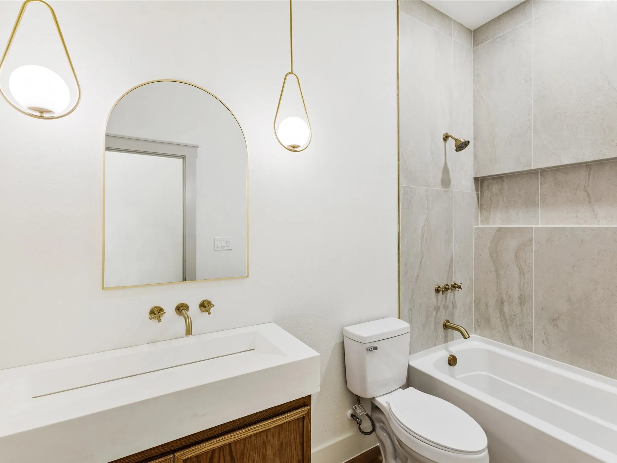 Wall-mounted brass fixtures, an arched vanity mirror, and drop pendant lighting