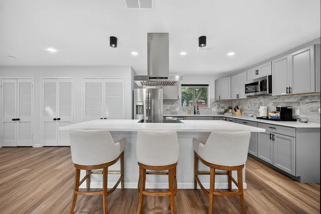 Modern kitchen featuring a large central island, wood-finish flooring, light gray cabinetry, and stainless steel appliances