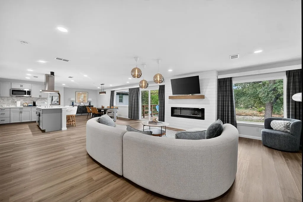 Open-concept living area featuring wood-finish flooring, a contemporary fireplace with a wood mantle, and recessed lighting