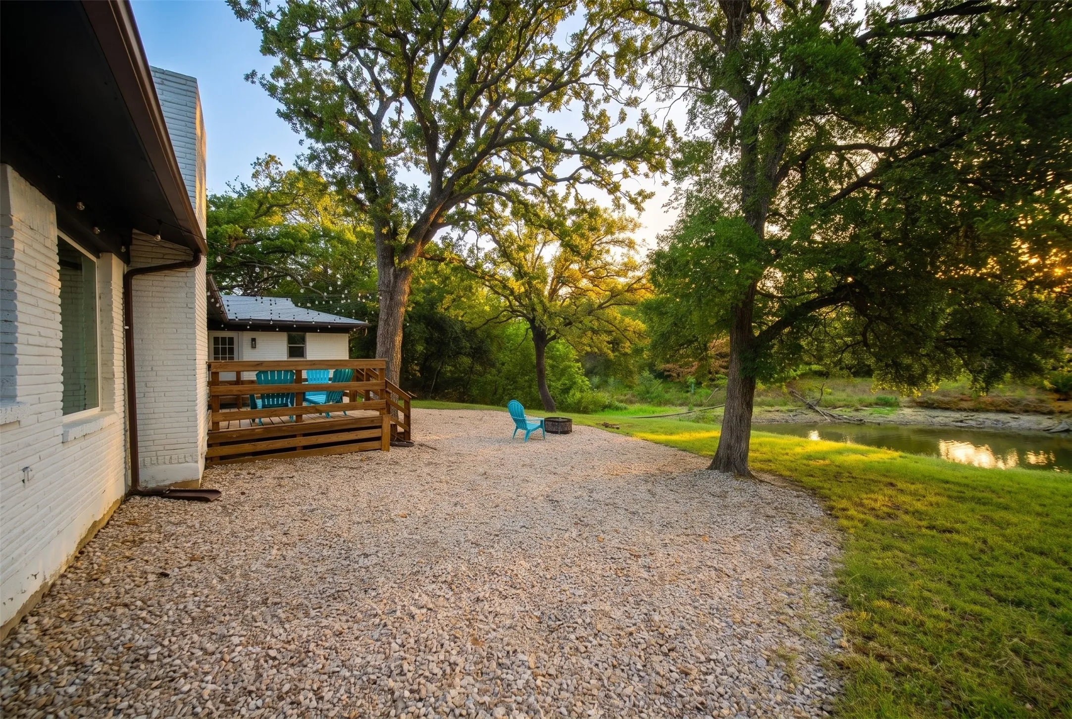 Wood deck with horizontal railing, gravel patio, mature trees, and natural waterfront