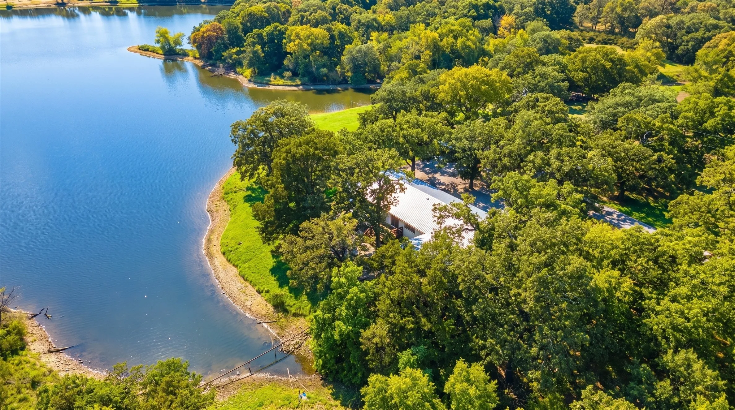 Waterfront property featuring a structure with a light-colored roof, surrounded by extensive mature trees and natural landscaping
