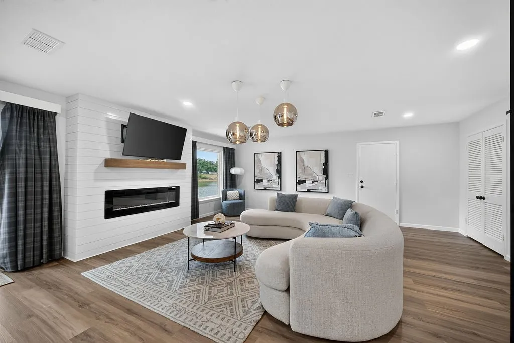 Shiplap accent wall with a linear fireplace, wood-finish flooring, recessed lighting, and a window with water scenery