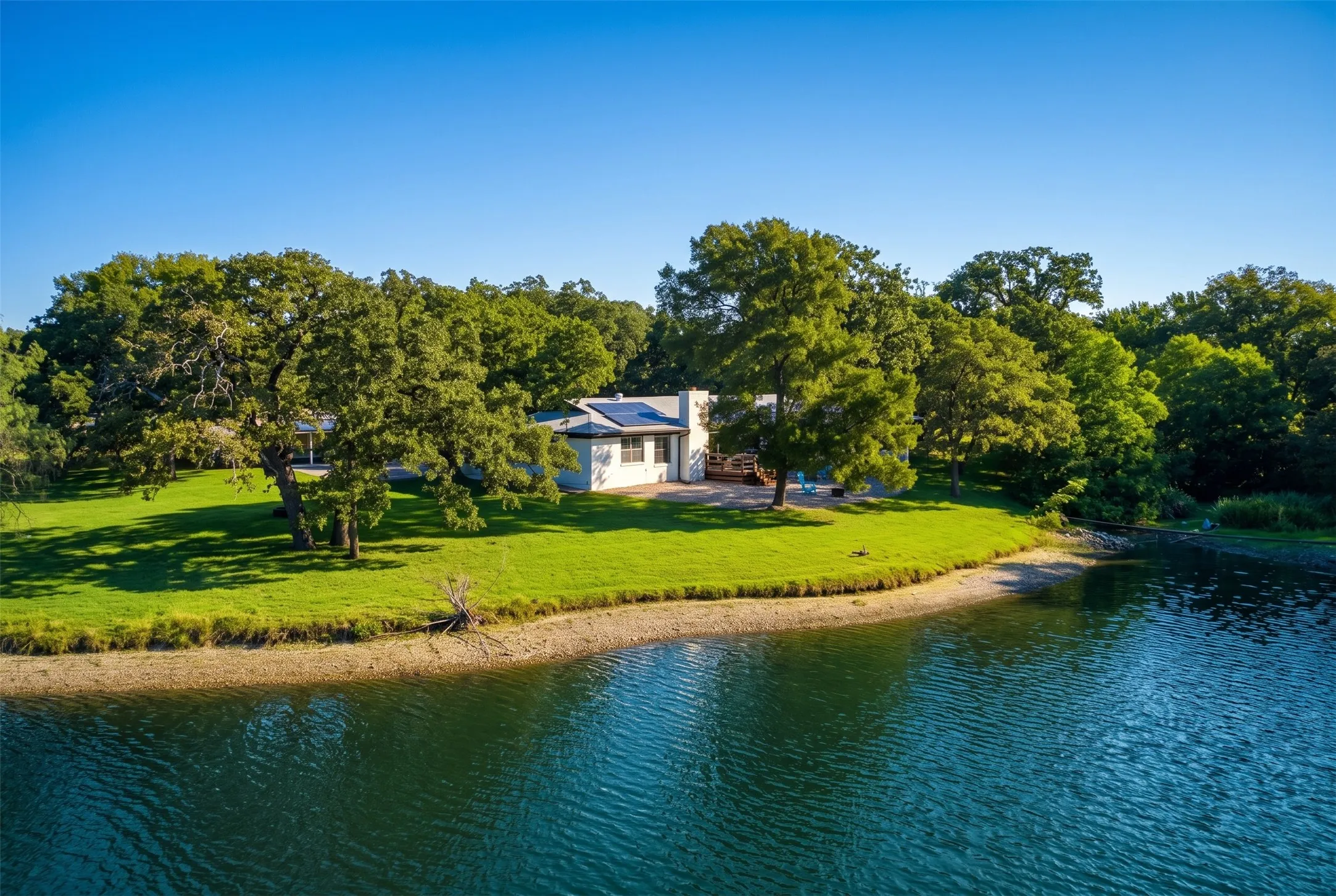 Lakeside property featuring a white exterior, solar panels, and mature trees