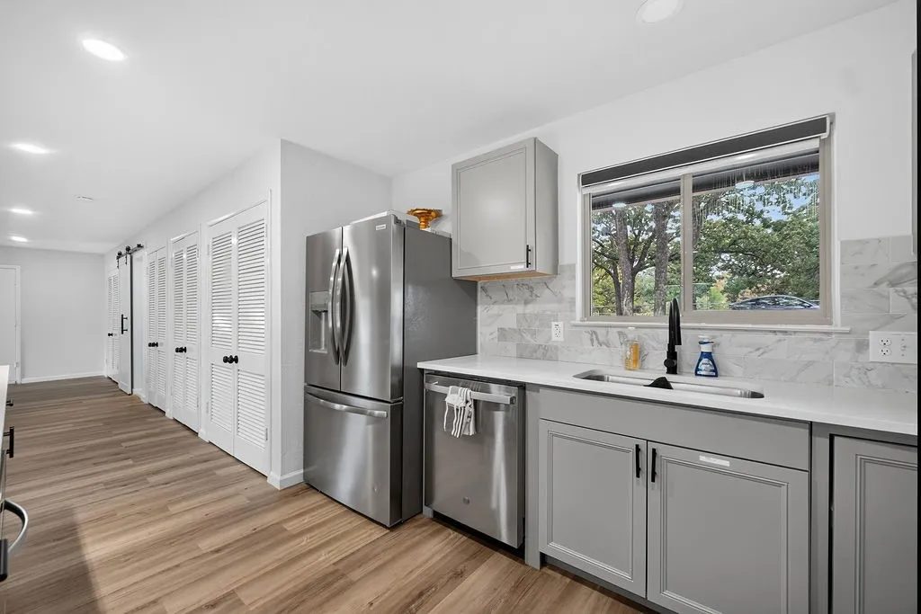 Contemporary kitchen featuring stainless steel appliances, light gray cabinetry, wood-finish flooring, a matte black faucet, and a tiled backsplash