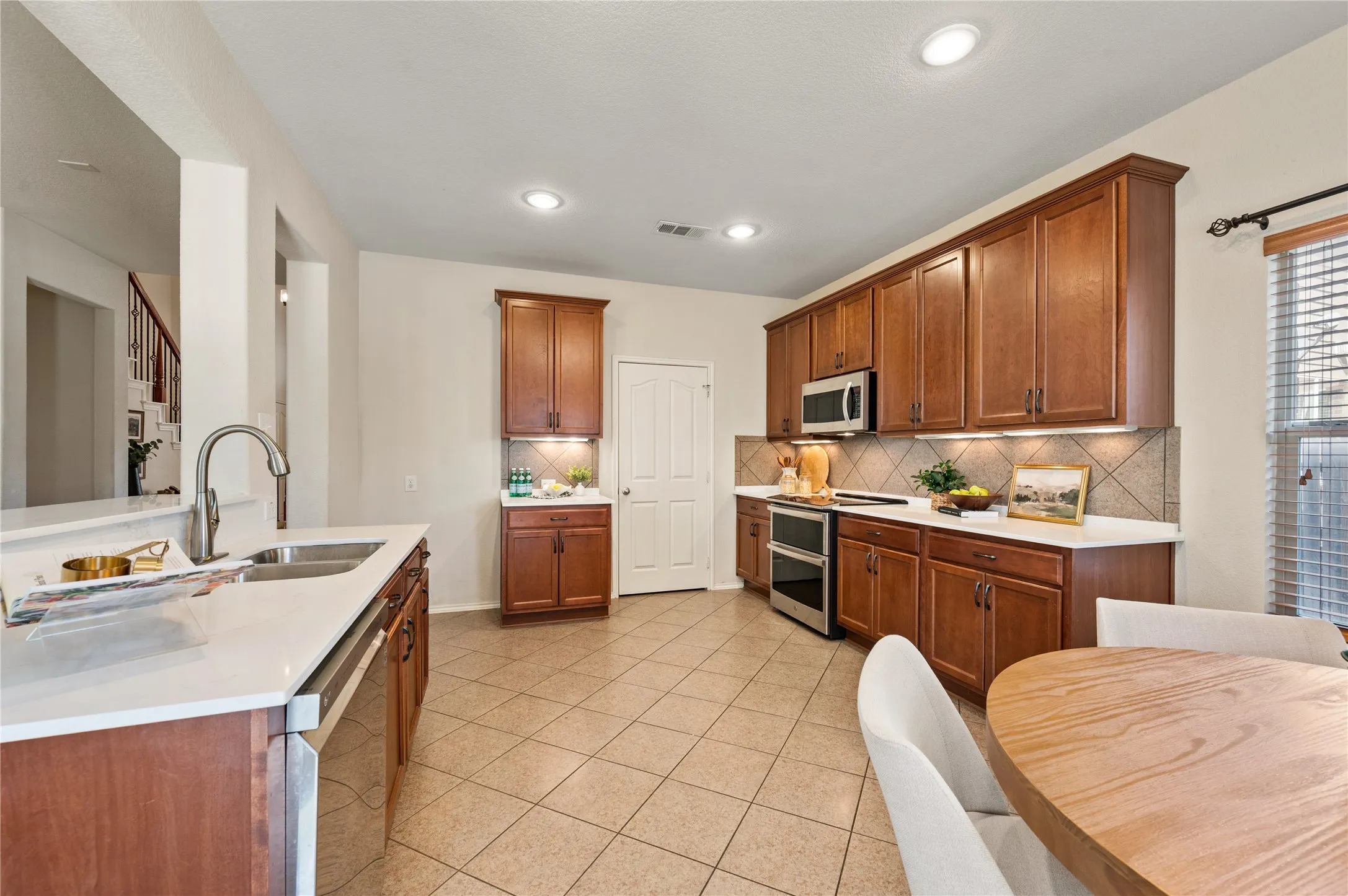 Kitchen featuring wood cabinetry, stainless steel appliances, white countertops, tile backsplash, and recessed lighting