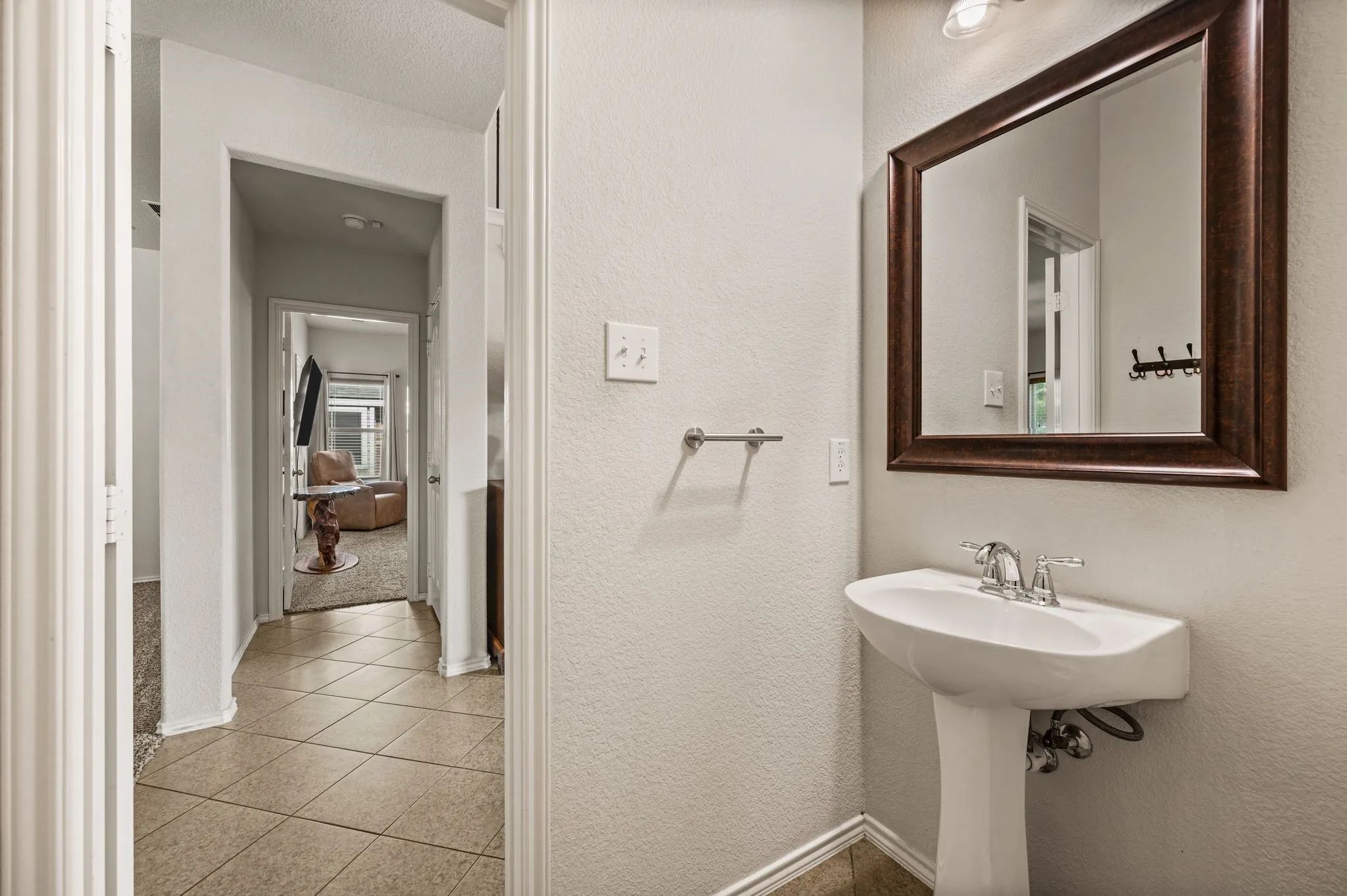 Pedestal sink with chrome faucet, framed mirror, and tile flooring