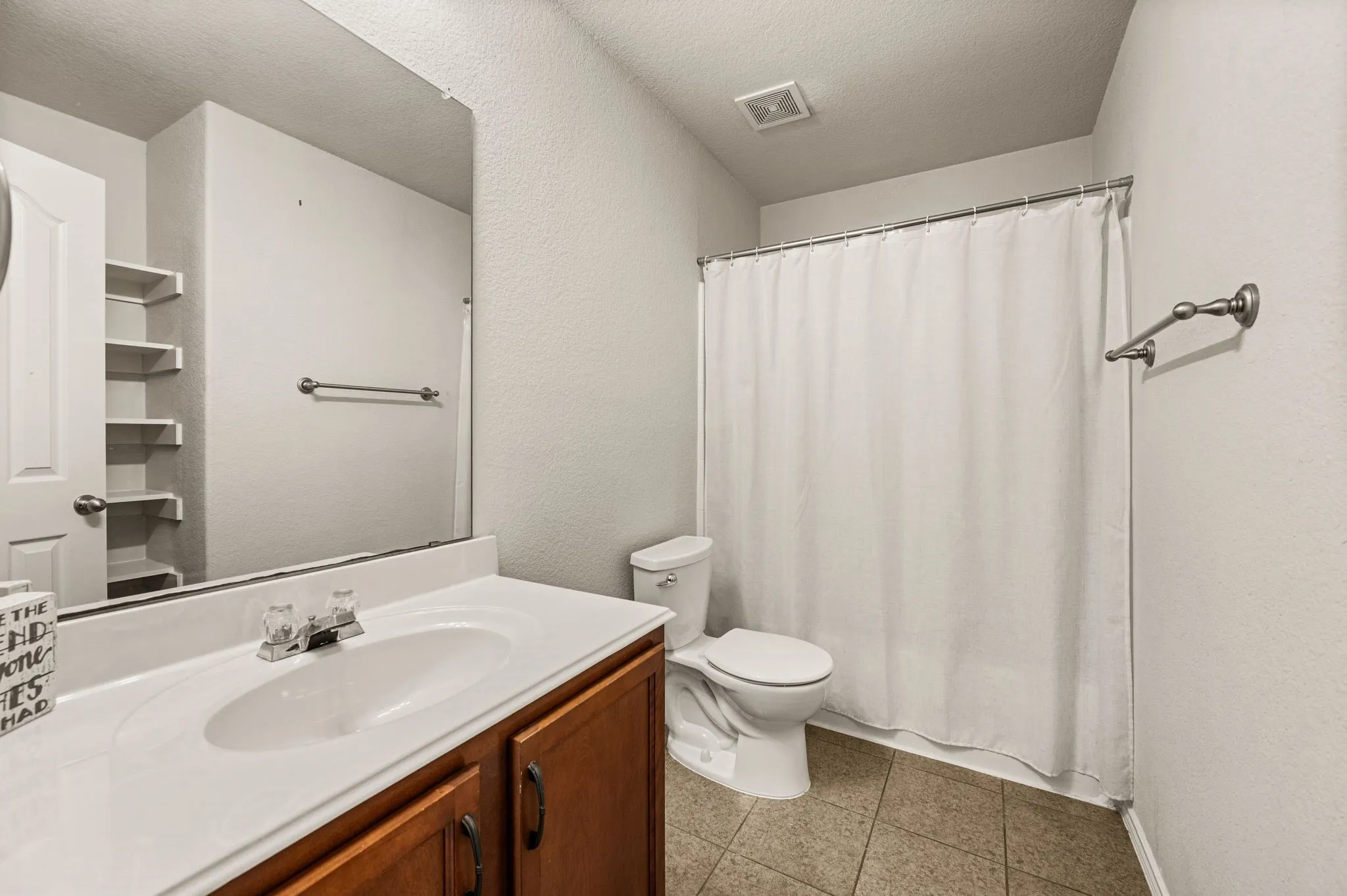 Bathroom featuring a wood-finish vanity, integrated sink, large wall-mounted mirror, built-in shelving, and tiled flooring