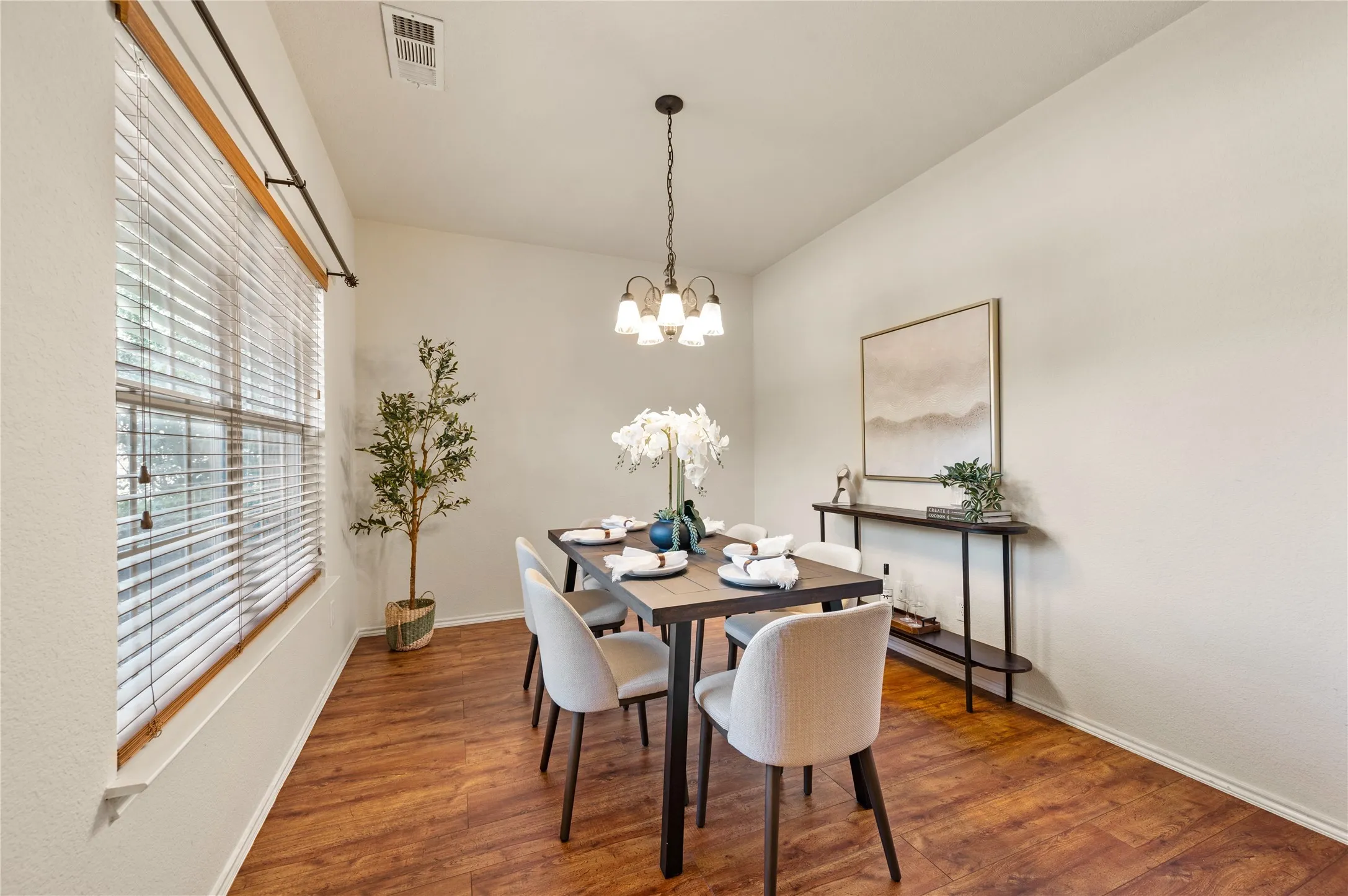 Spacious dining area featuring wood-finish flooring, a large window with blinds, and an overhead chandelier
