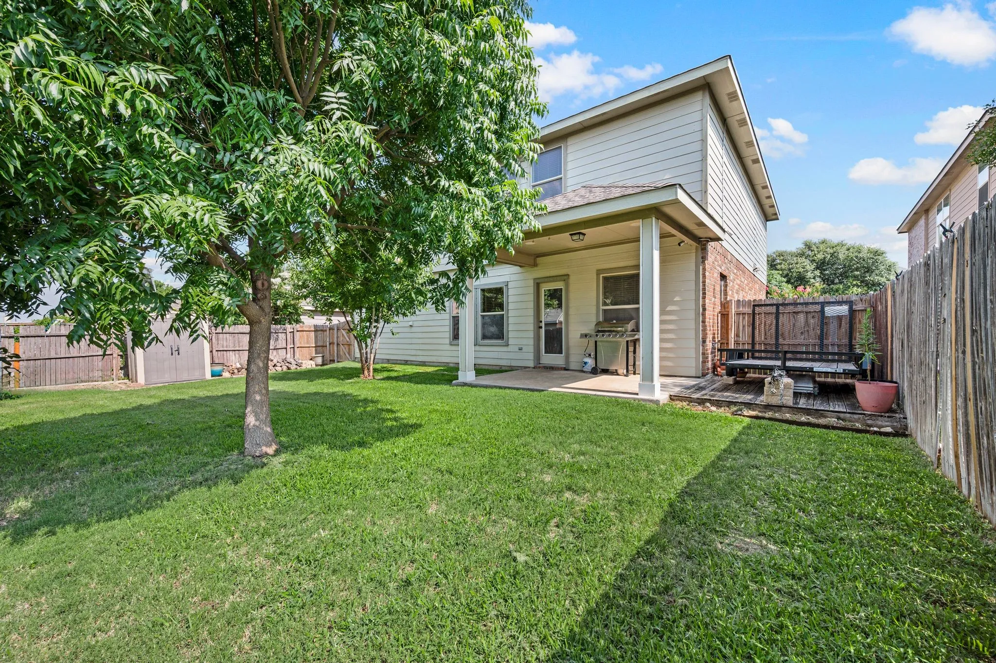 Expansive backyard featuring a covered patio, a wood deck, a mature tree, and a storage shed