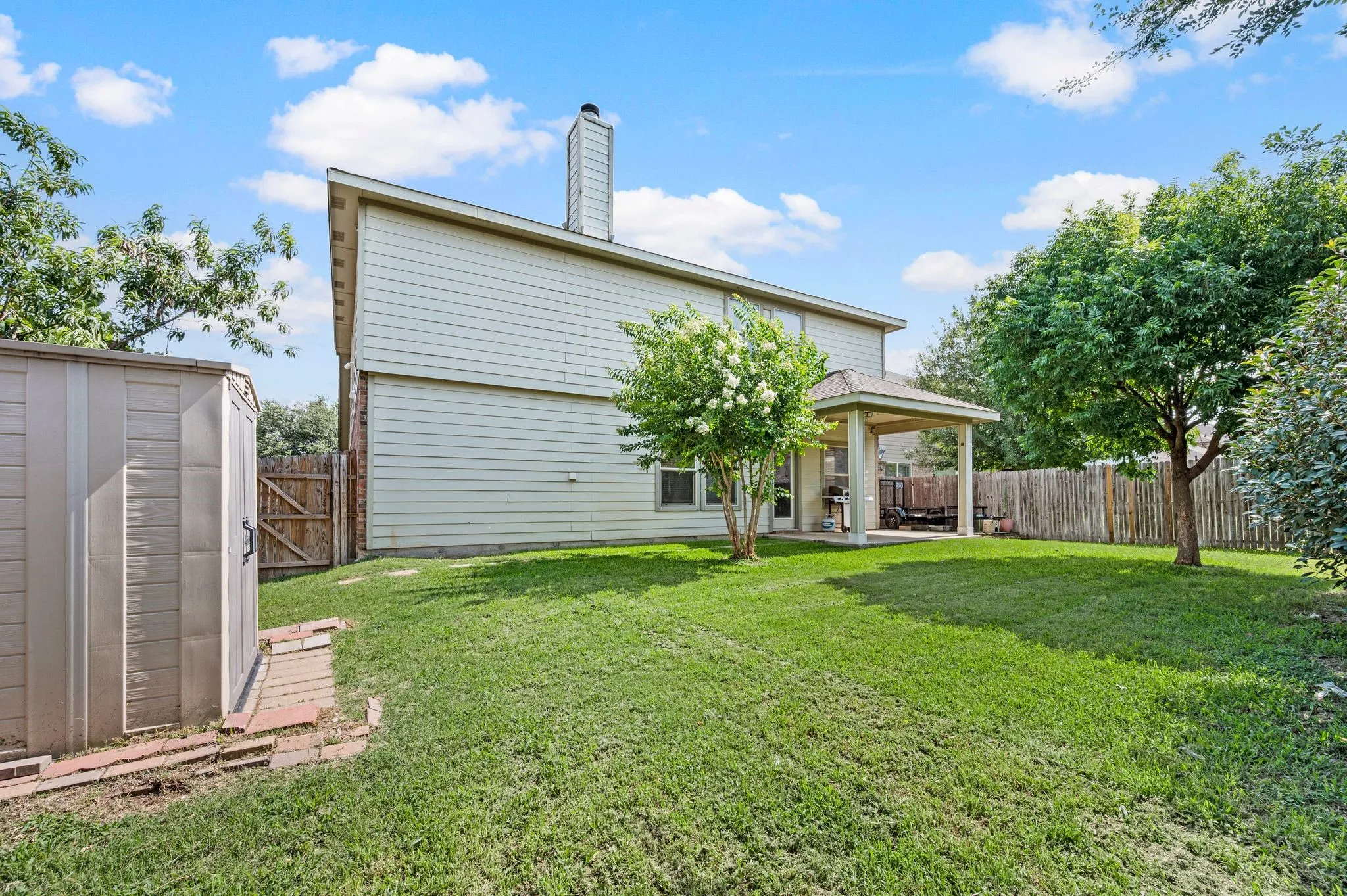 Expansive backyard featuring a covered patio, a storage shed, a wood privacy fence, and mature trees