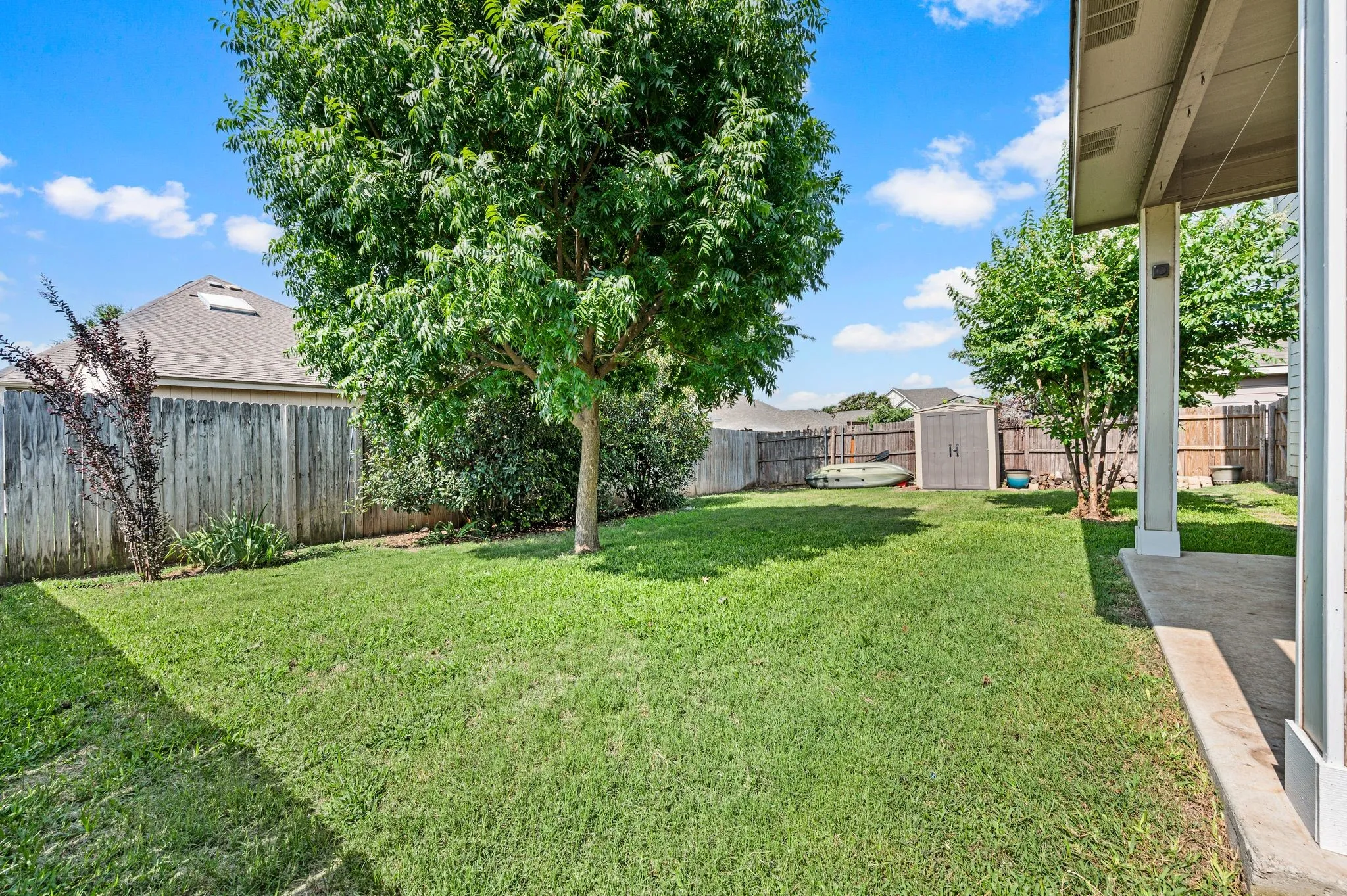 Expansive backyard featuring a manicured lawn, established trees, wood fencing, and a concrete patio