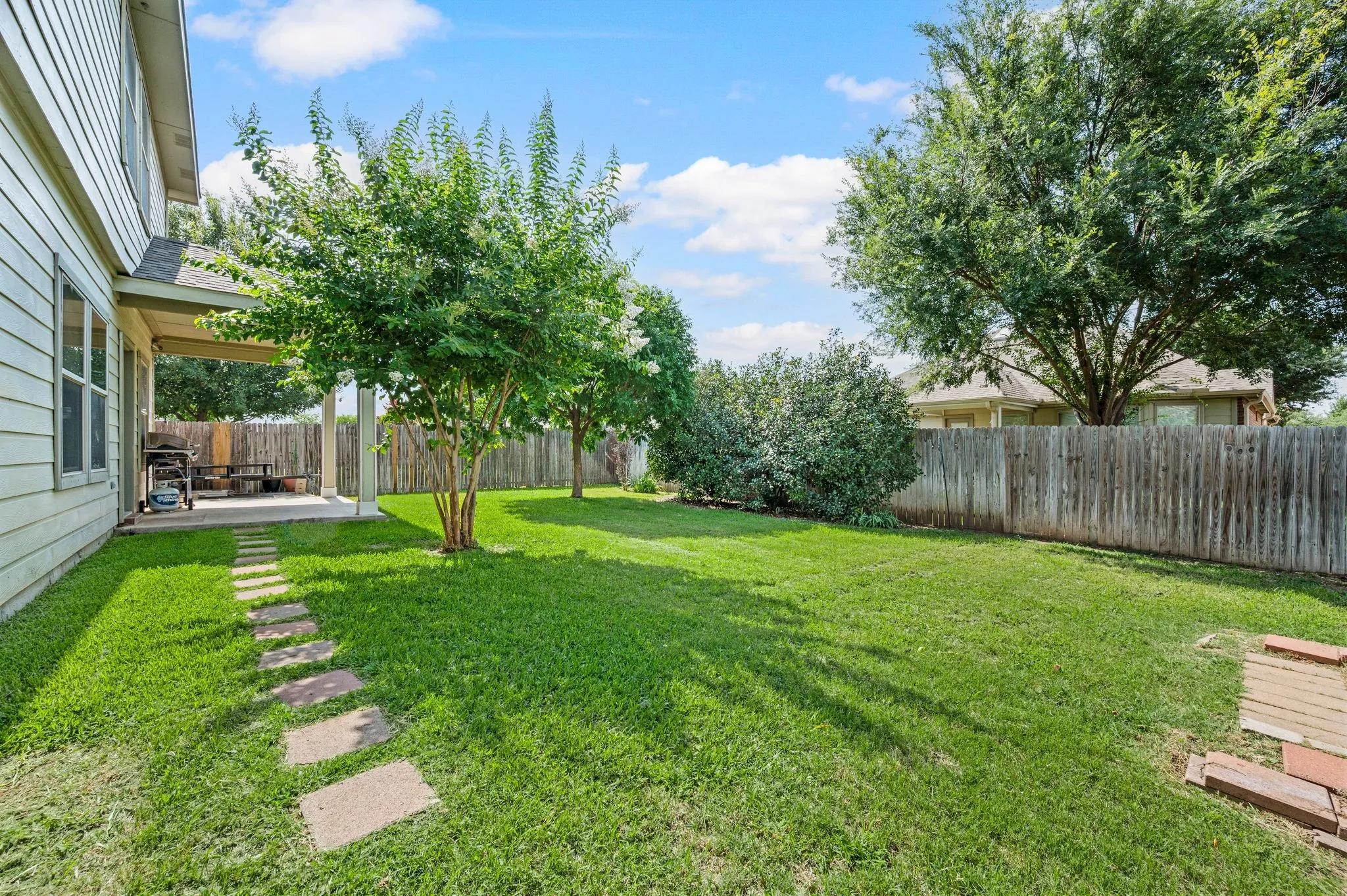 Expansive backyard featuring a lush lawn, a covered patio, and a wood privacy fence